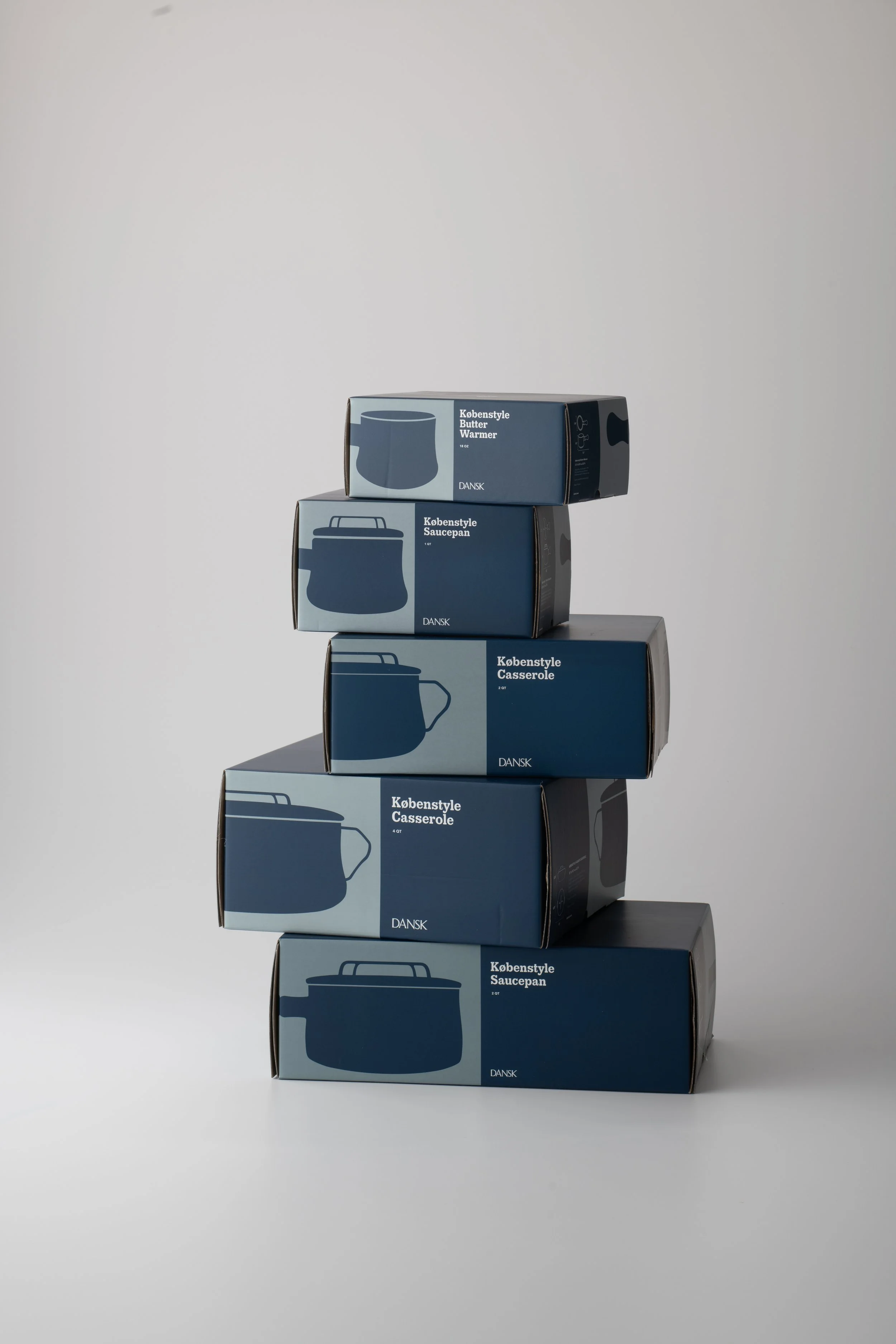 Stack of five blue and black boxes labeled with different kitchenware items, arranged in a descending tower on a gray surface with a plain light gray background.