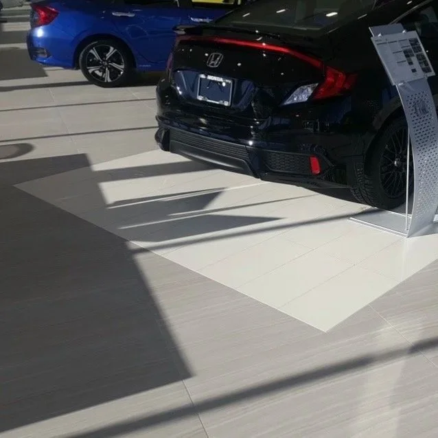 Black Honda car displayed in a showroom with a blue car visible in the background and a white display stand to the side.