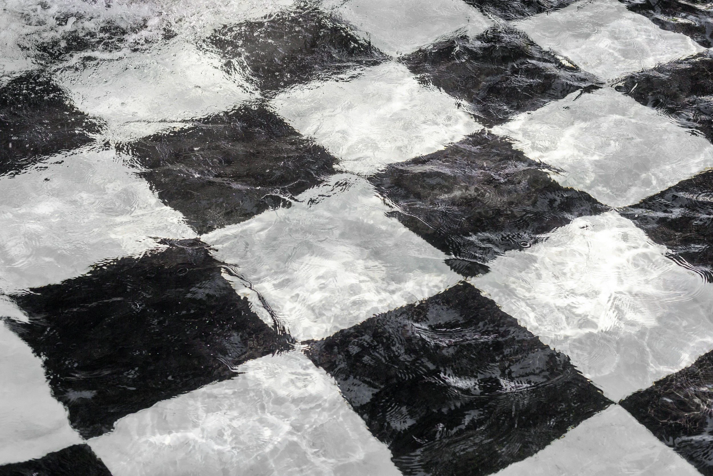 Close-up of wet, dark rocks partially submerged in water with small ripples and reflections.