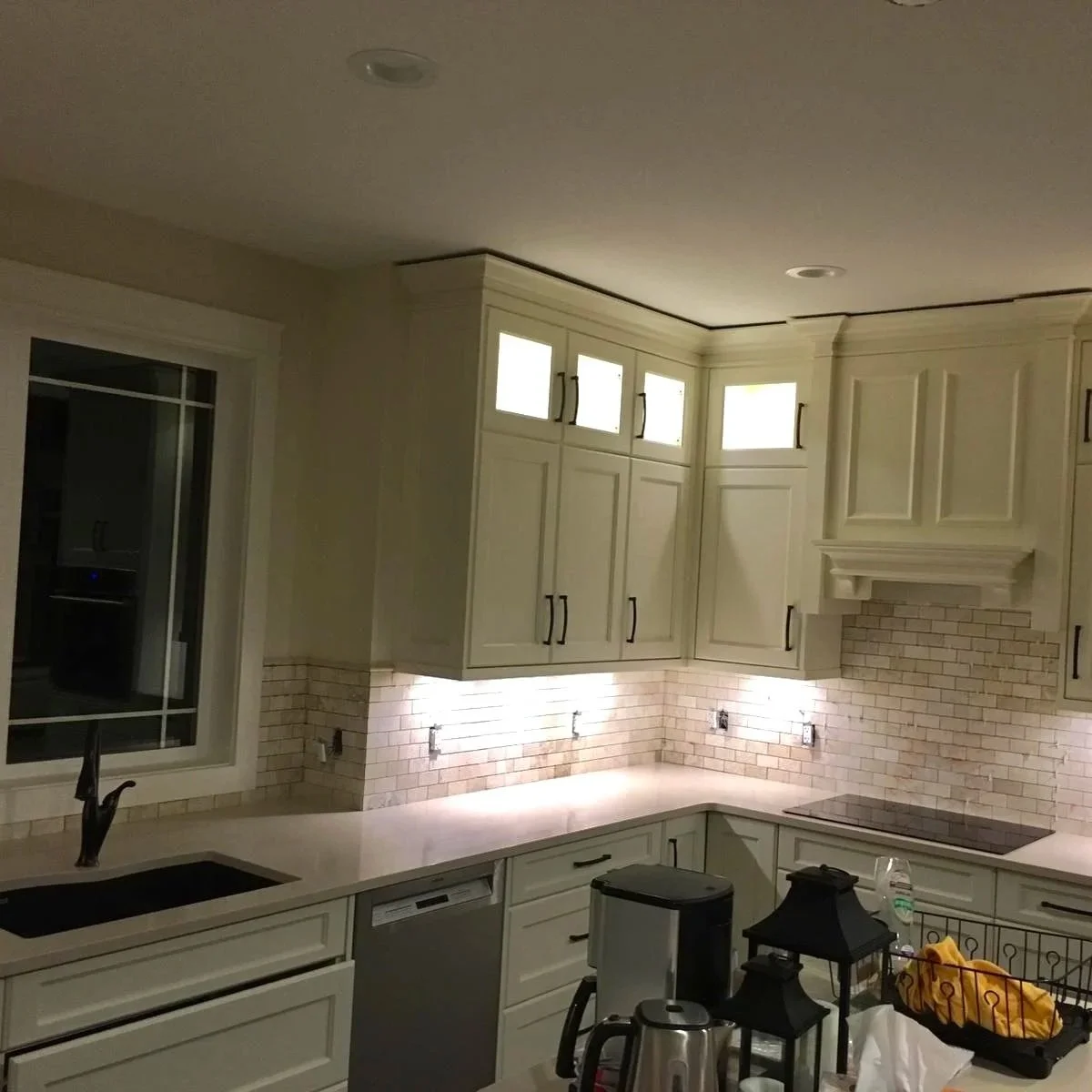 Kitchen with cream-colored cabinets, white subway tile backsplash, under-cabinet lighting, window above sink, and an electric cooktop on the counter.