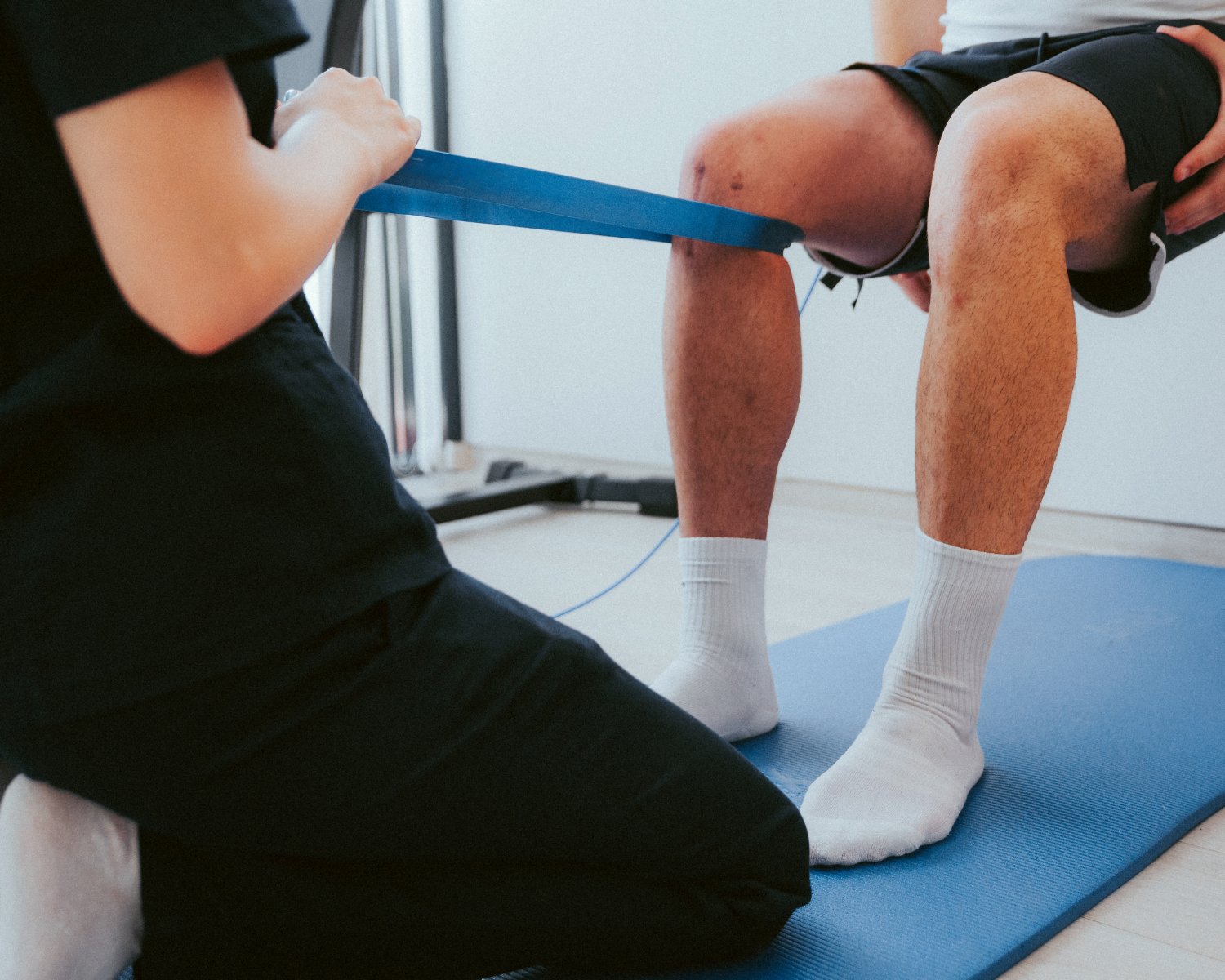 Person doing physical therapy exercises with resistance band while kneeling on a blue exercise mat.