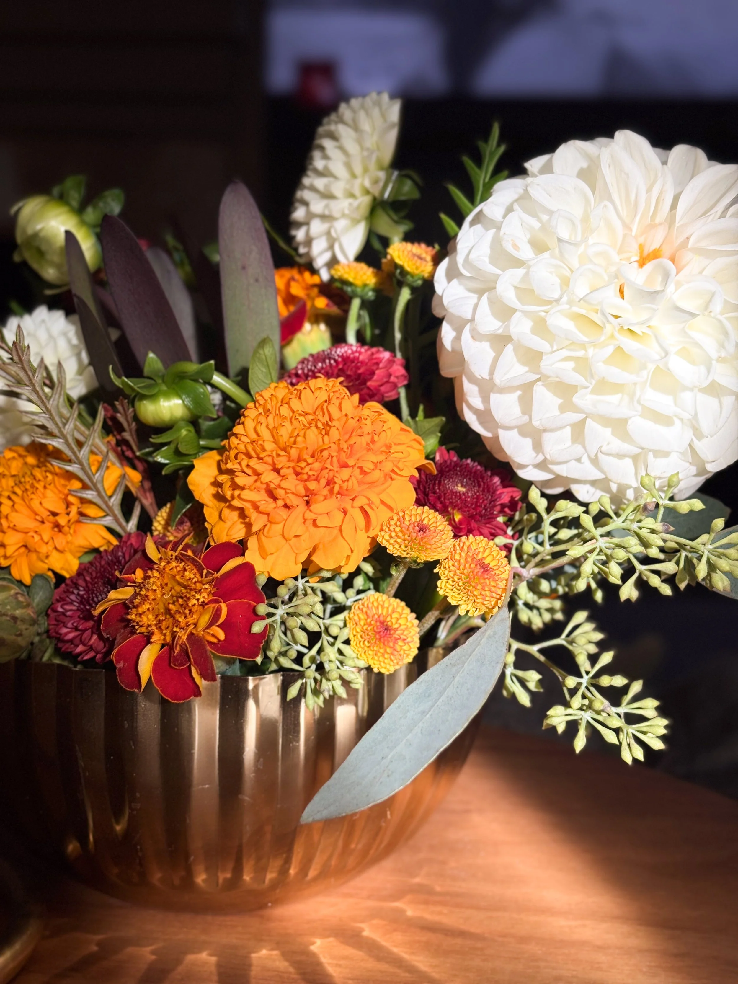 A bouquet of various colorful flowers in a metallic container on a wooden surface.