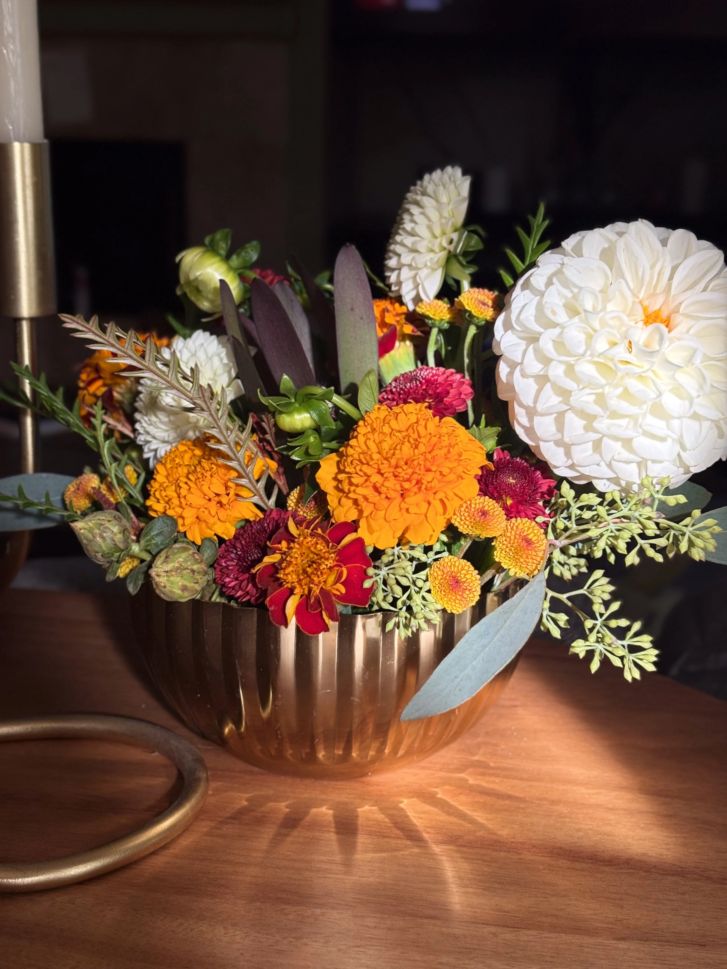 A bouquet of mixed flowers in a metallic vase on a wooden surface, with a dark background.