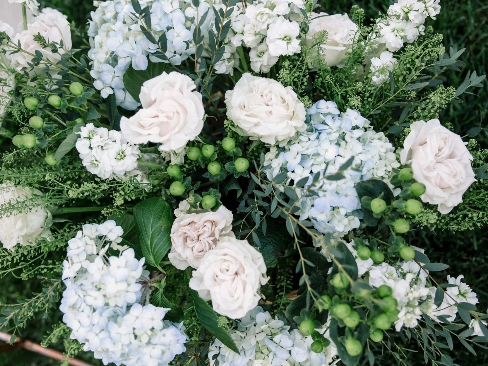 A bouquet of white roses, hydrangeas, and green berries with greenery.