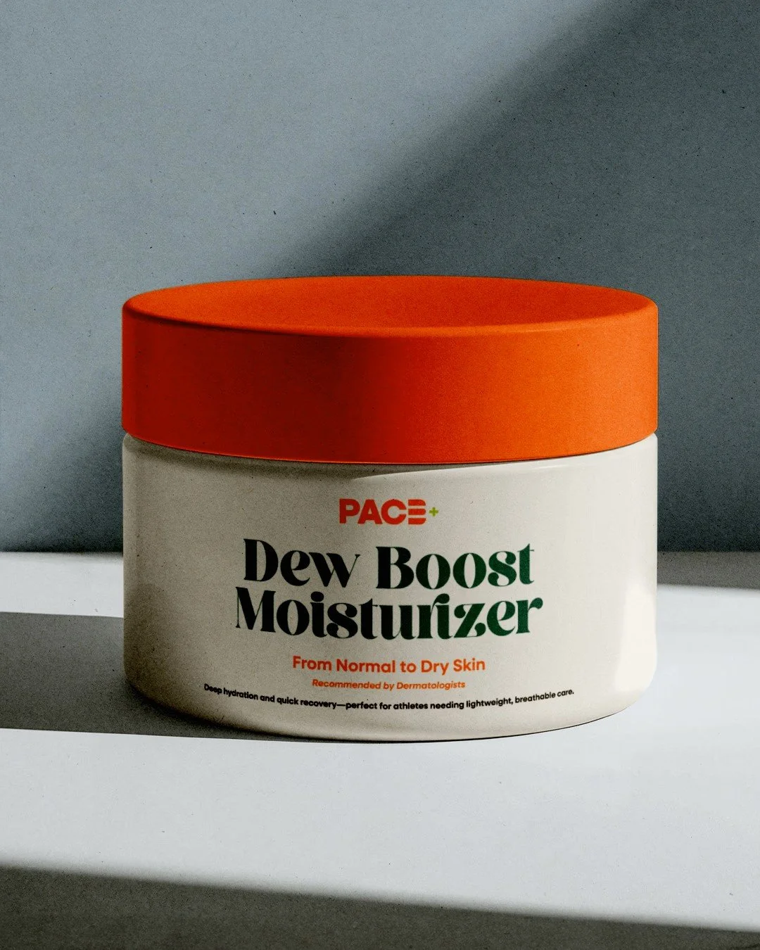 A container of PACE Dew Boost Moisturizer with an orange lid and white body, labeled for dry skin and recommended by dermatologists, placed on a white surface with shadows.
