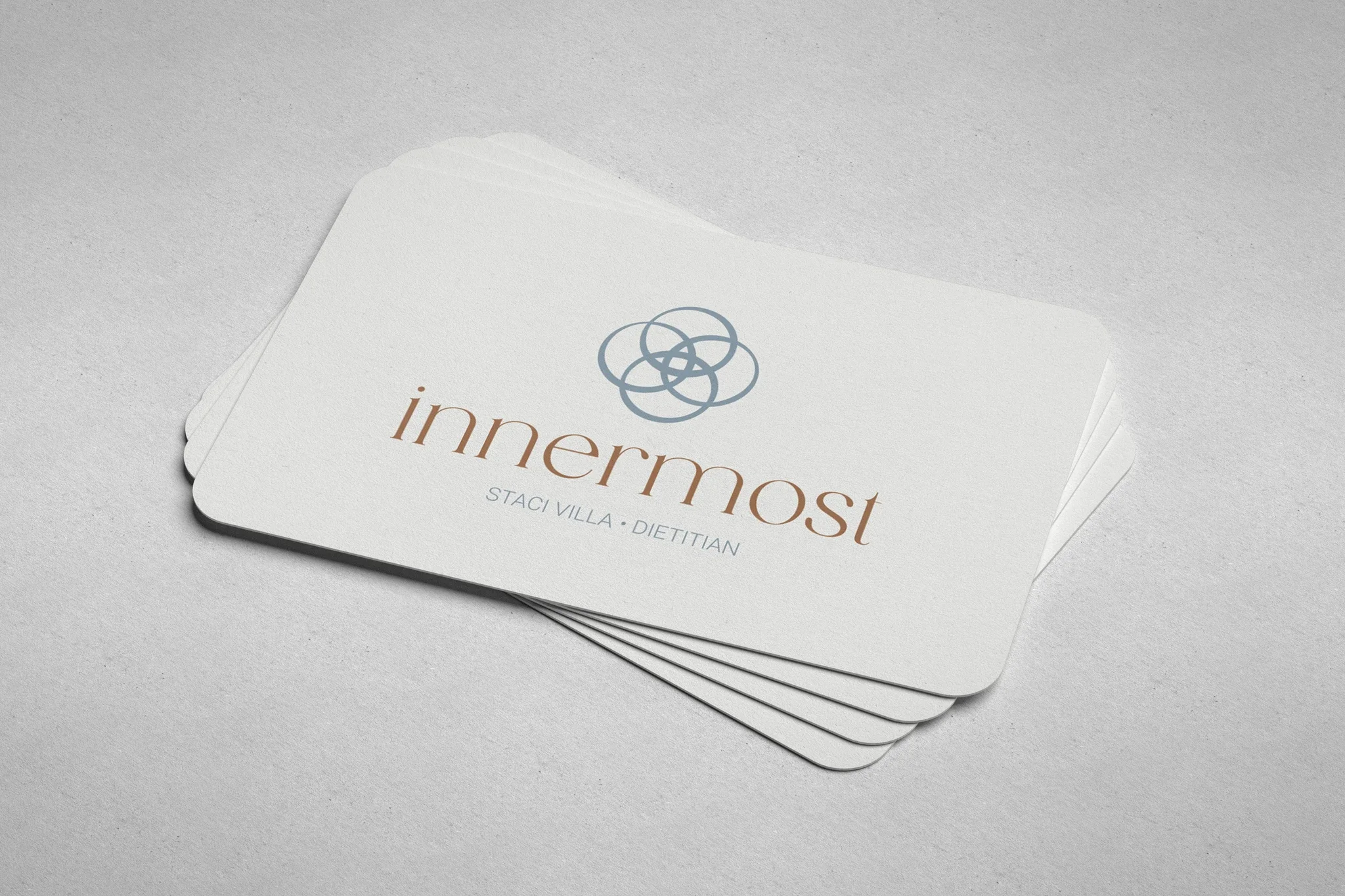 A stack of white business cards on a textured gray surface, featuring the logo and name 'innermost' in brown and gray text, along with the designer's name Staci Villa, a dietitian.