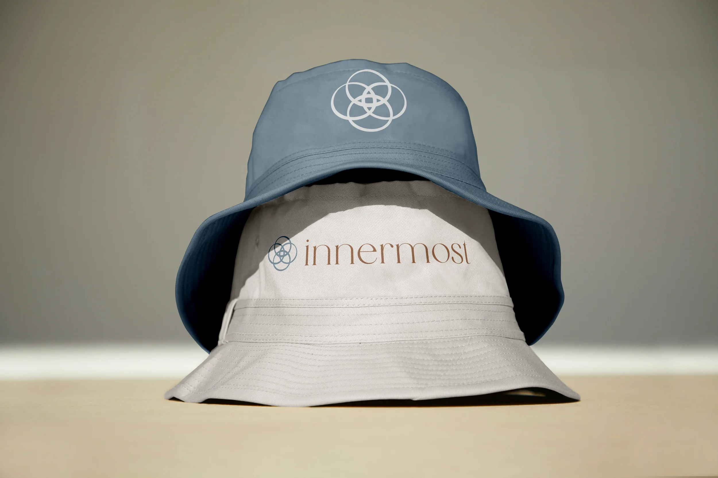 A blue baseball cap on top of a white hat, both with the logo and name of Innermost, positioned on a flat surface against a neutral background.