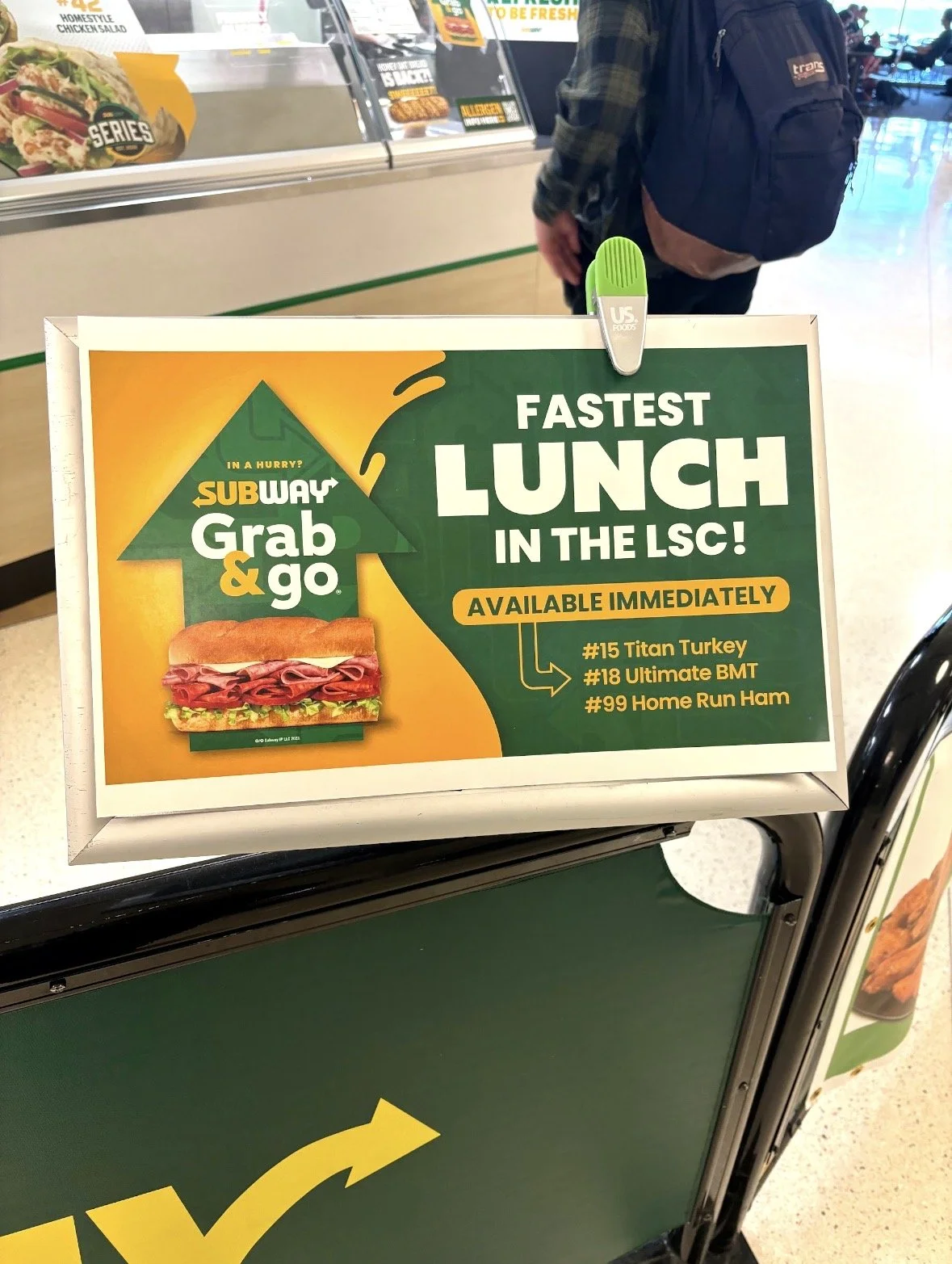 Sign advertising Subway Grab & Go lunch options, highlighting the fastest lunch in the local service center, available immediately. Featuring a picture of a sandwich with meats and vegetables. Items include Titan Turkey, Ultimate BMT, and Home Run Ha