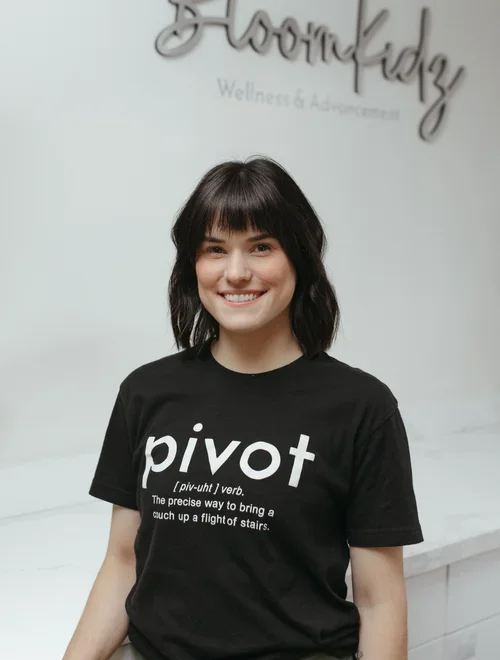 A young woman with shoulder-length dark hair and bangs, smiling, wearing a black t-shirt with the word pivot and its definition on a white background.