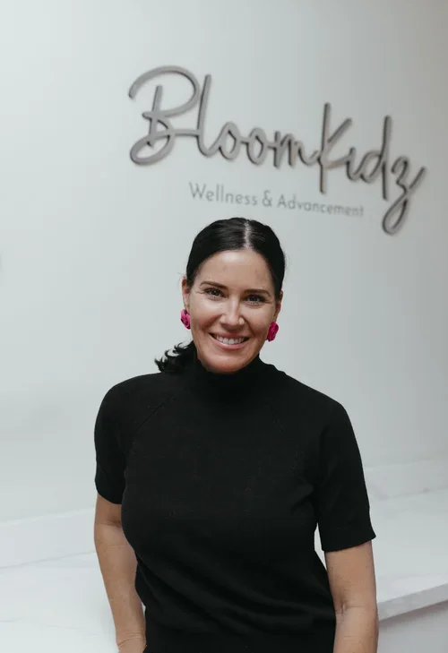 Woman smiling in front of a sign that says 'Bloomkidz Wellness & Advancement'.