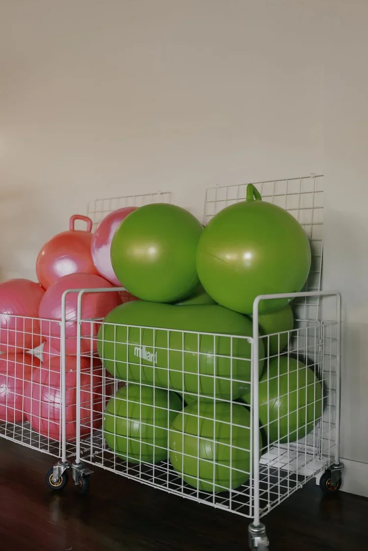 Green exercise balls and pink exercise balls stored in white wire baskets on casters.