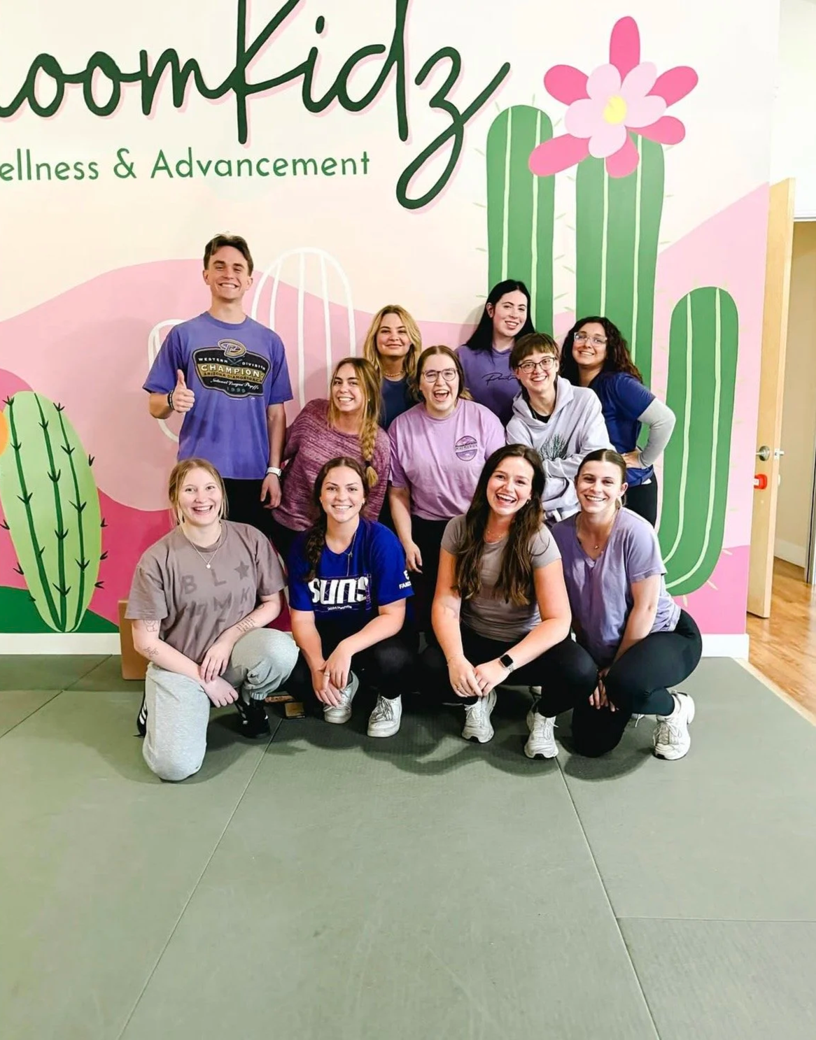 Group photo of 11 smiling people posing in front of a colorful cactus mural