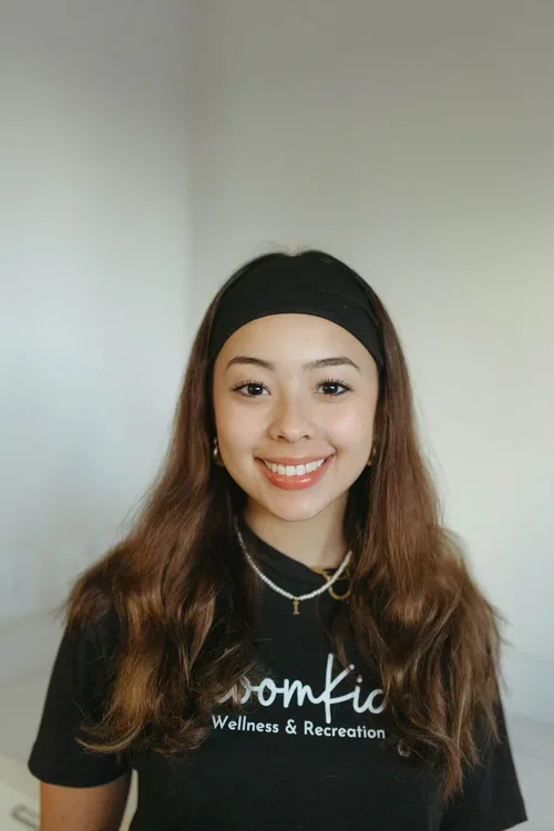 Smiling young woman with long brown hair wearing a black headband and Wellness & Recreation shirt