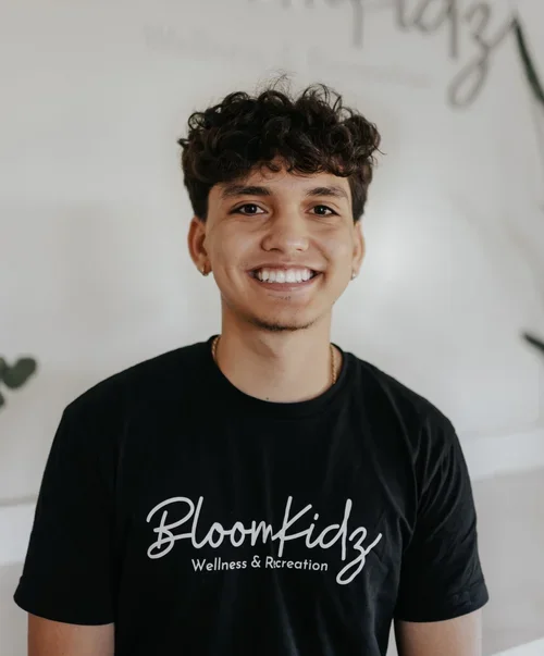 Young man with curly hair smiling, wearing a black t-shirt with 'BloomFiz' Wellness & Recreation written on it.