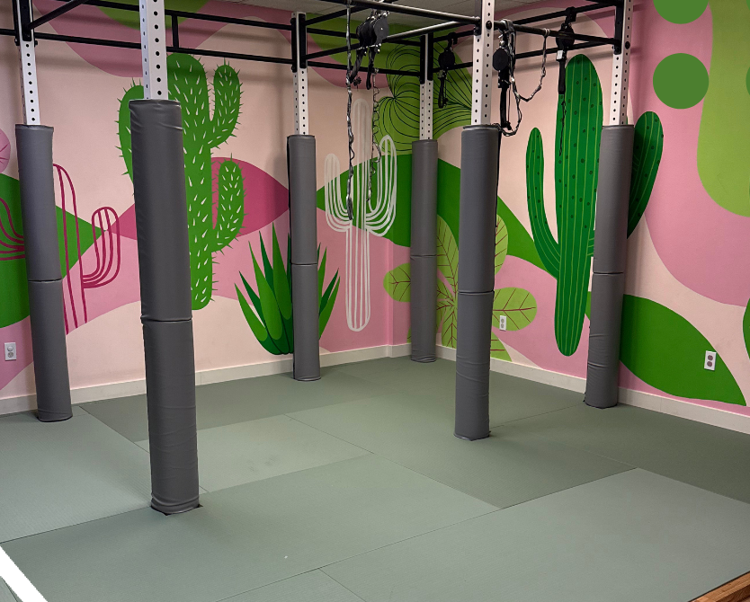 Indoor climbing area with padded floor and colorful cactus-themed wall mural.
