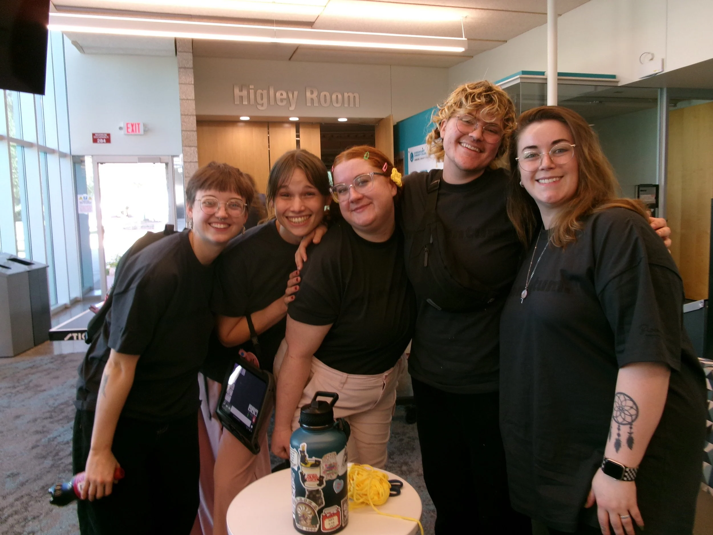 Five smiling people posing together in a building lobby outside the Higley Room.