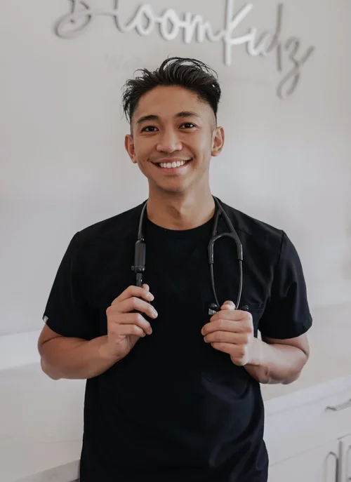Smiling young male healthcare professional holding a stethoscope in a clinic setting.