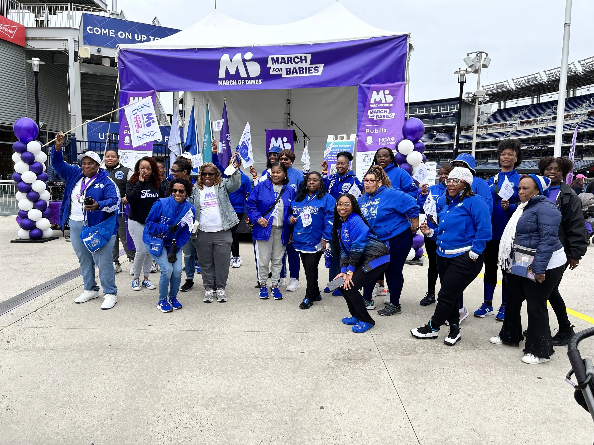 Group of people participating in a March for Babies event at a stadium, holding flags and wearing blue jackets.