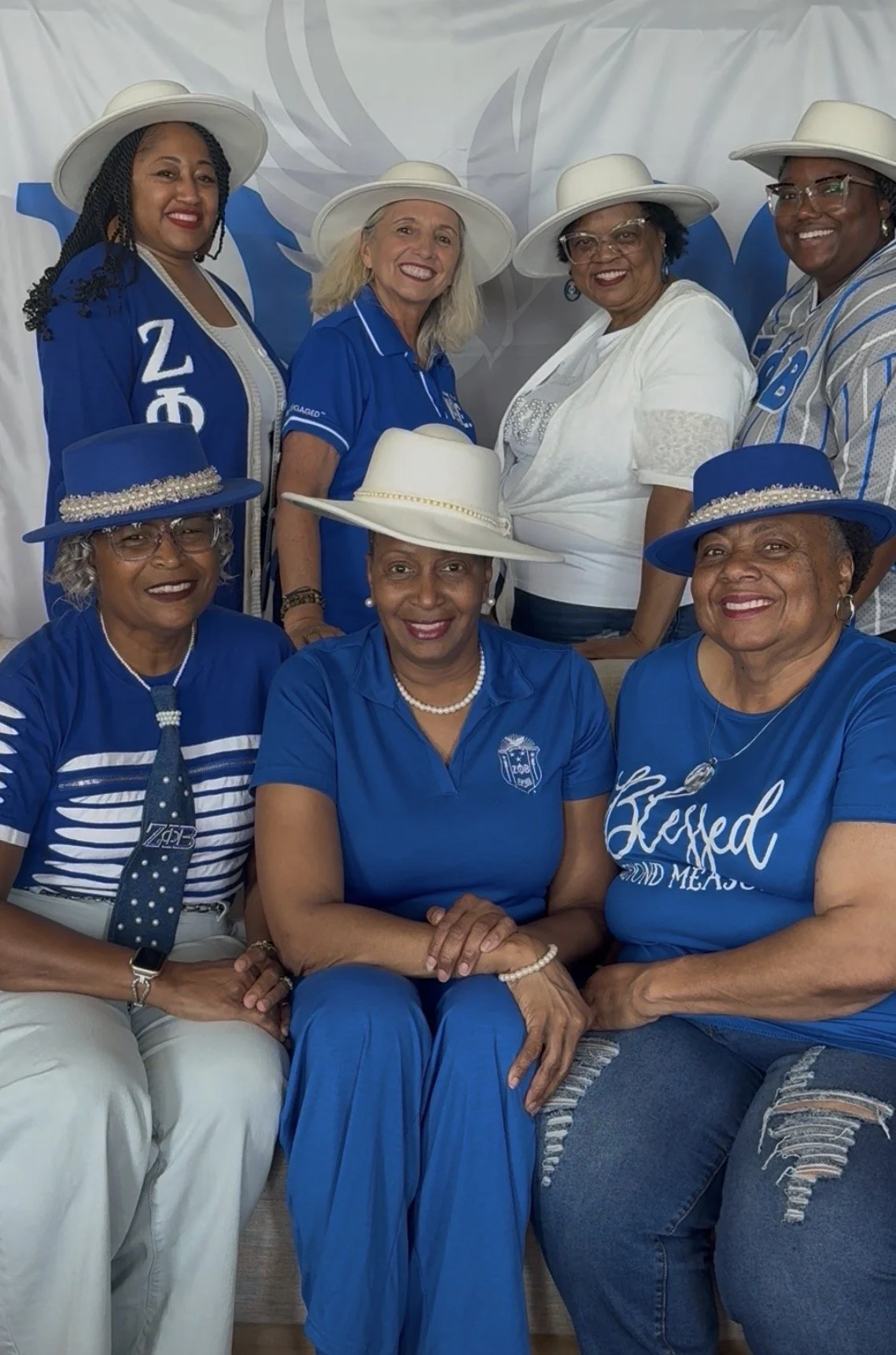 Group of women, mostly African American, smiling and wearing white hats and blue clothing, posing in front of a decorative backdrop with a white and blue eagle logo.