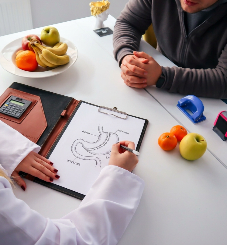 Un diagramme de l'estomac avec des annotations, plusieurs fruits comme des pommes, des oranges et des bananes, un calculateur, une perforatrice bleue et un individu en blouse blanche dans un contexte médical.