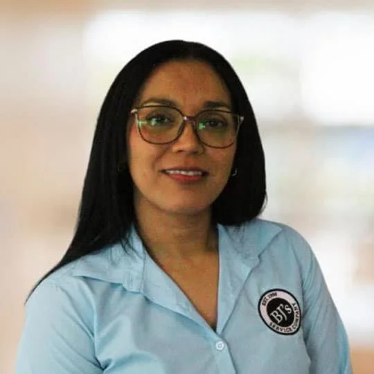 Woman with glasses and long dark hair wearing a light blue shirt with a logo on the chest.