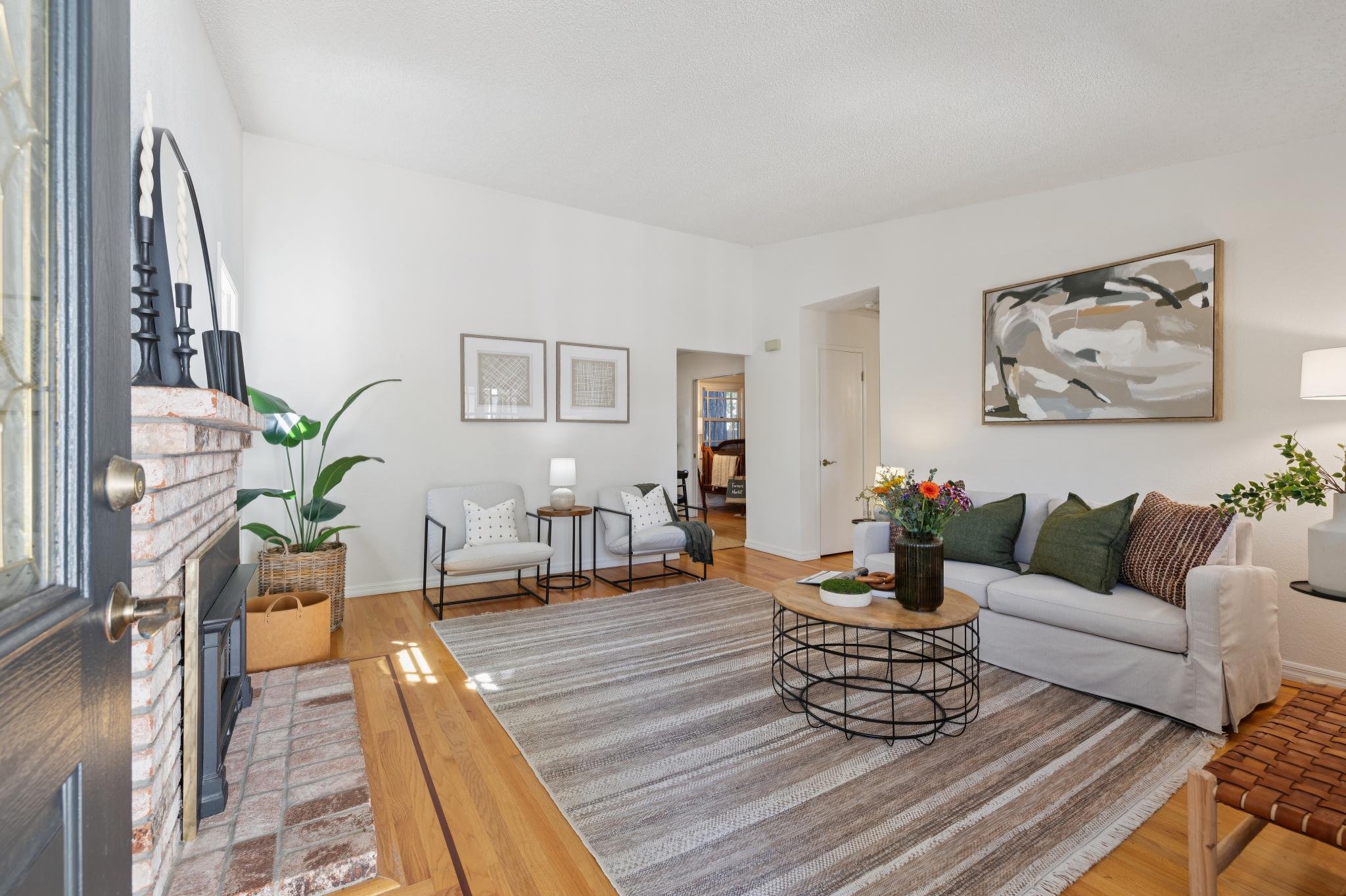 Living room with a white sofa, patterned cushions, a wooden coffee table with a vase of flowers, wall art, a striped area rug, a fireplace with candlesticks, and seating area.