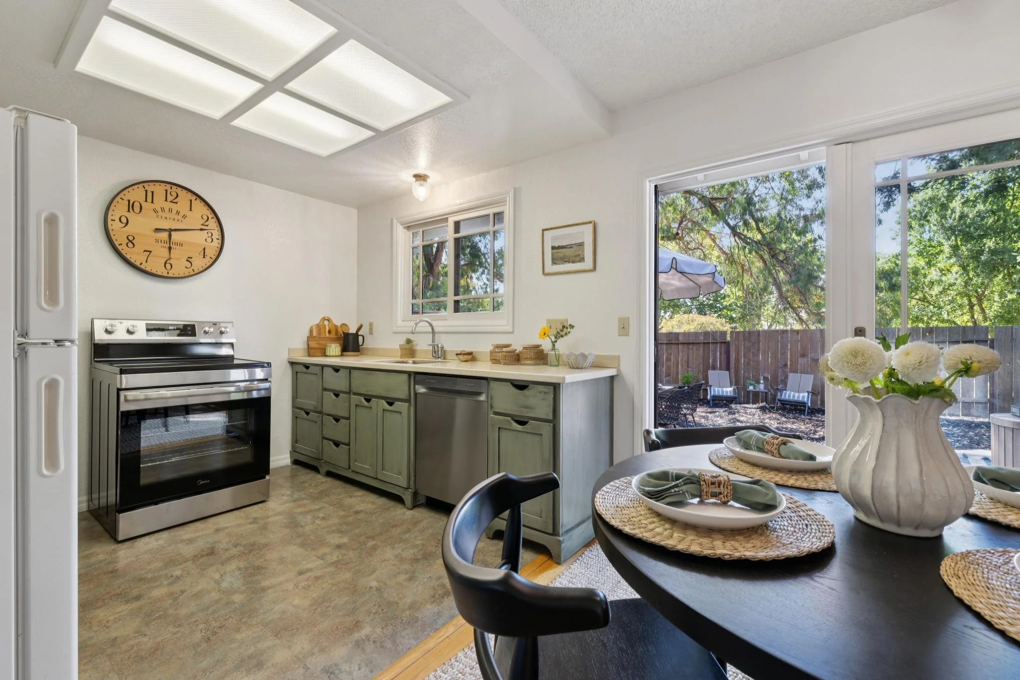 Kitchen with stainless steel oven, white cabinets, window, and sliding door leading to outdoor patio with chairs and trees