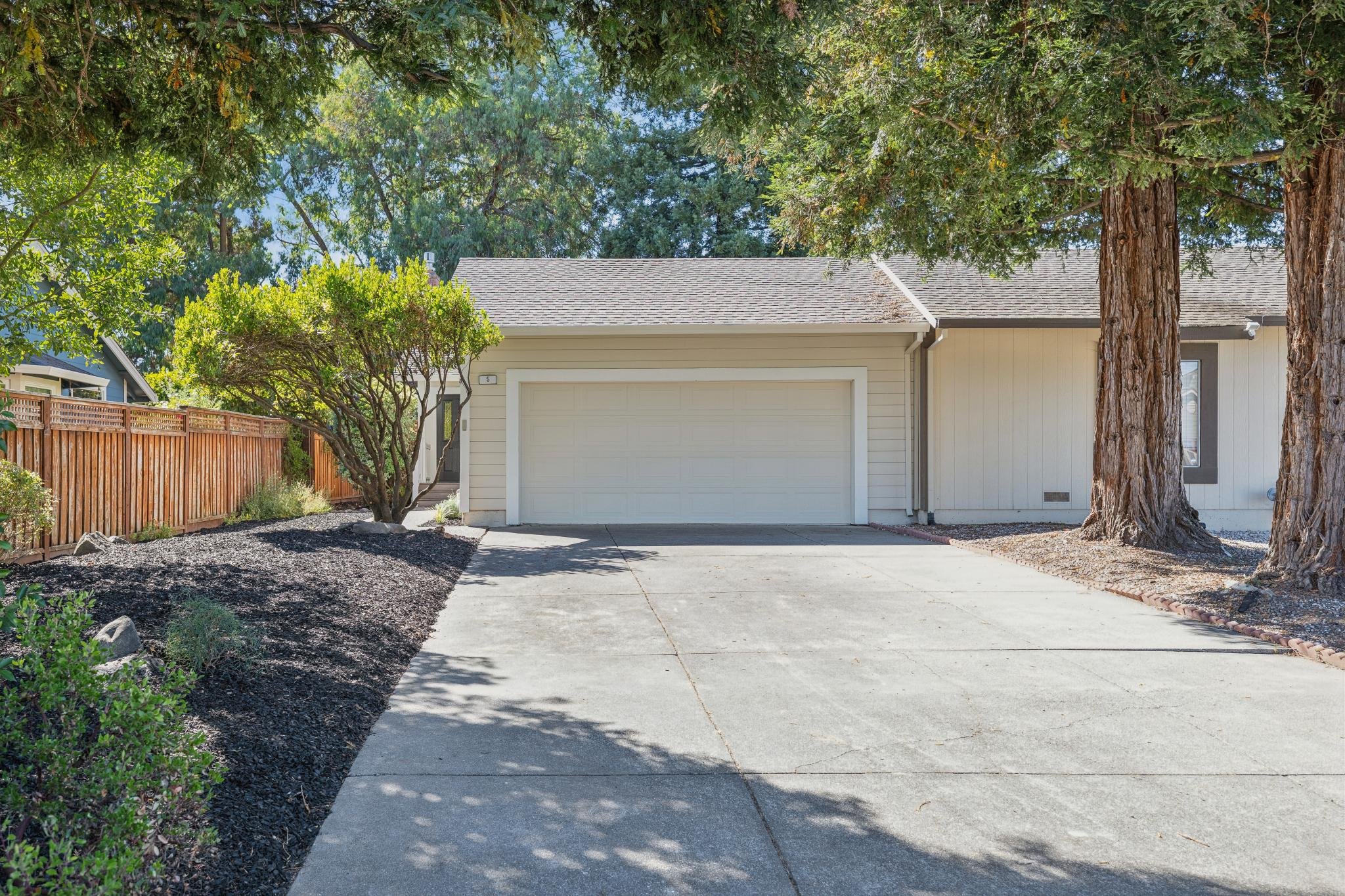 Front view of a house with a white garage door, surrounded by trees and a landscaped yard, in a suburban neighborhood.