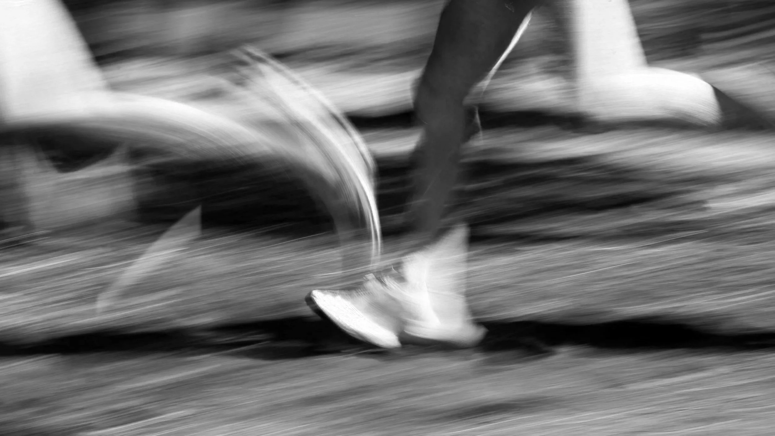 Blurred black-and-white image of a person running, focusing on legs and feet, with motion lines indicating fast movement.