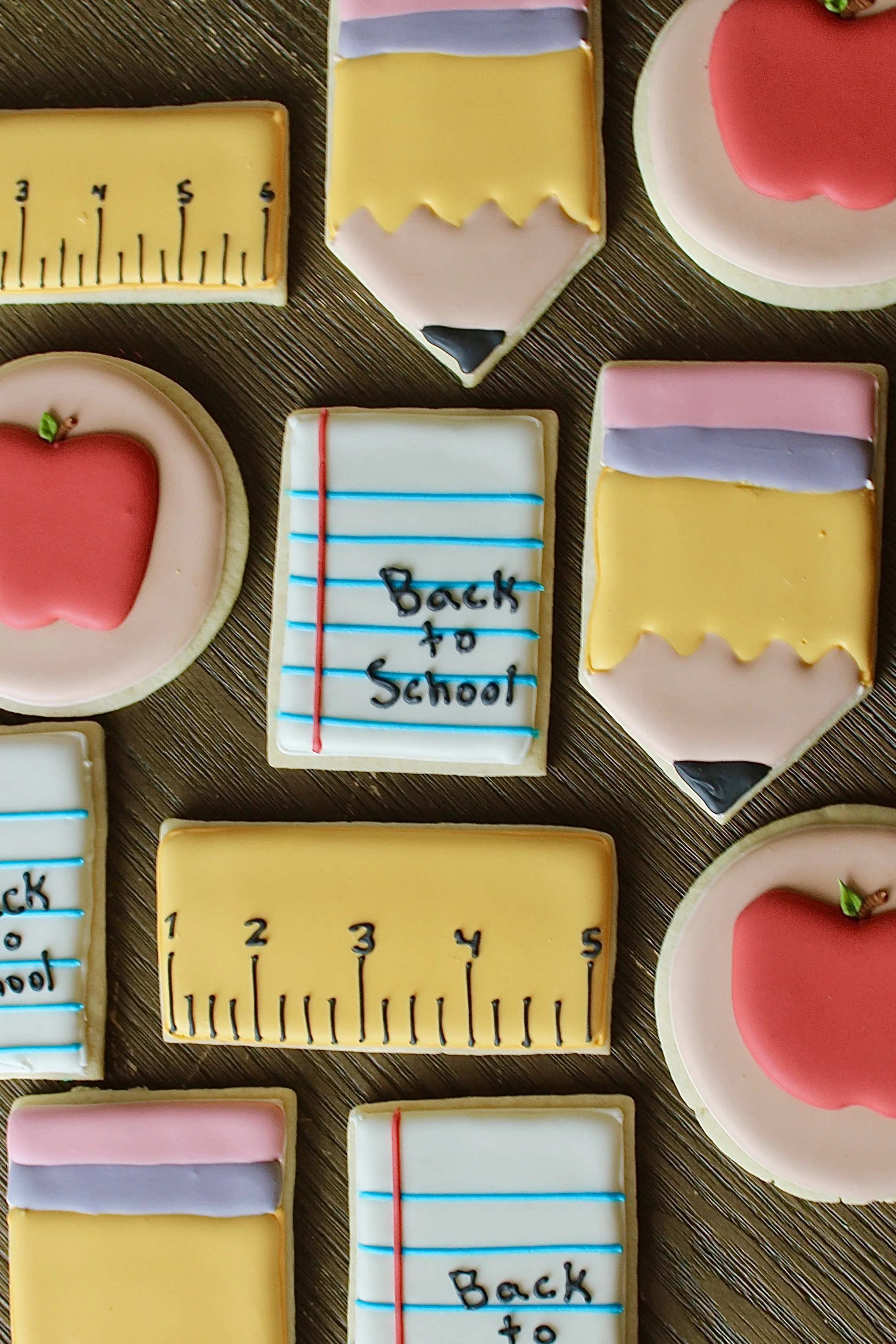 Decorated sugar cookies with school-themed designs, including pencils, a ruler, a notebook with 'Back to School' written on it, and apples.