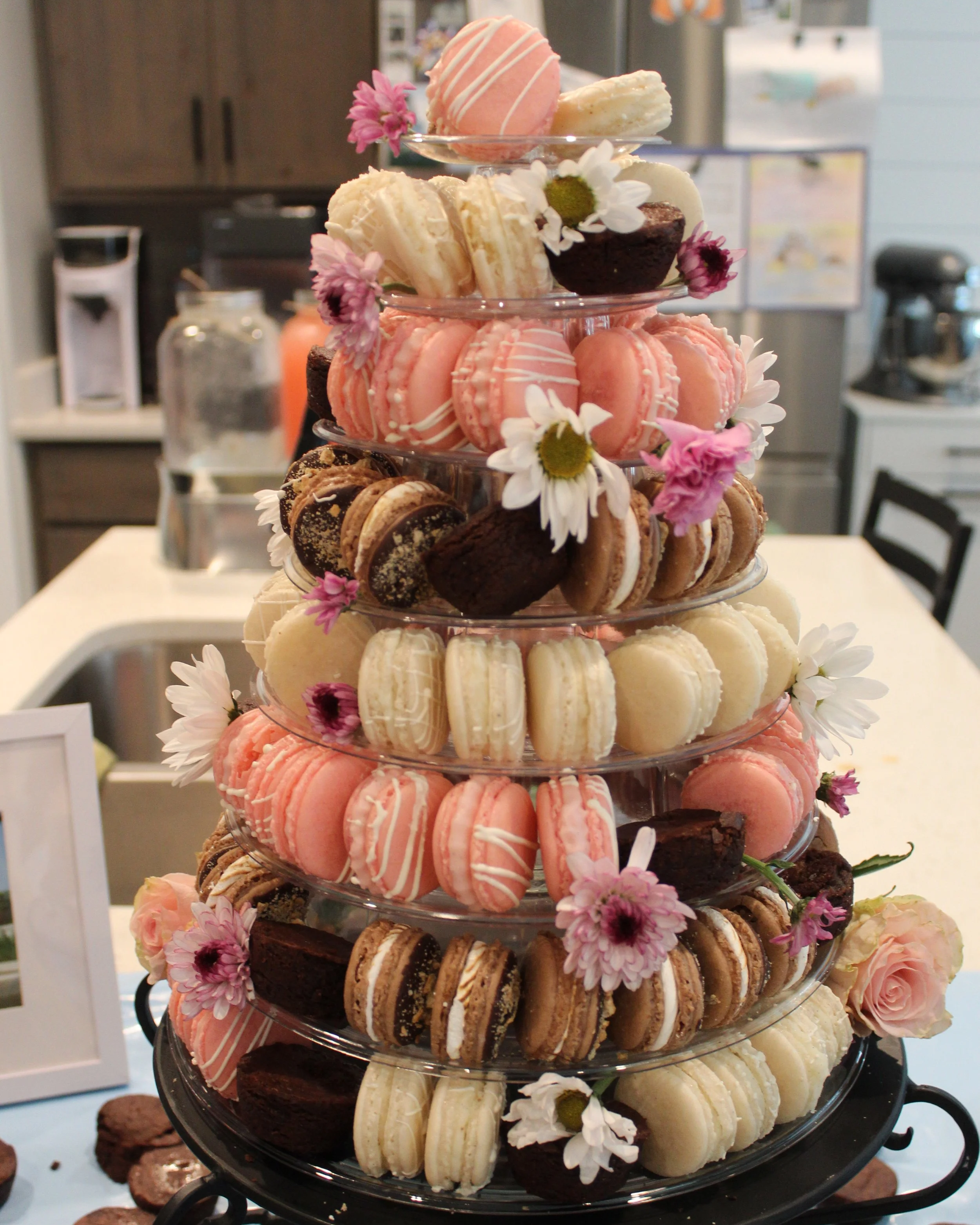 A tiered stand filled with assorted macarons, decorated with pink and white flowers.