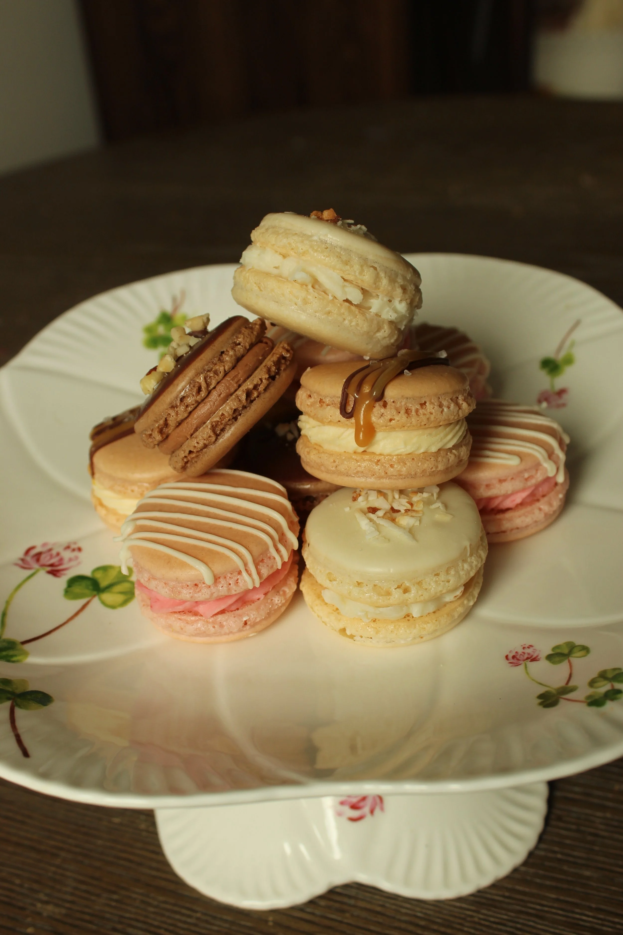A porcelain plate with pink, white, and brown macarons, decorated with chocolate, caramel, and nuts, arranged in a pyramid formation.
