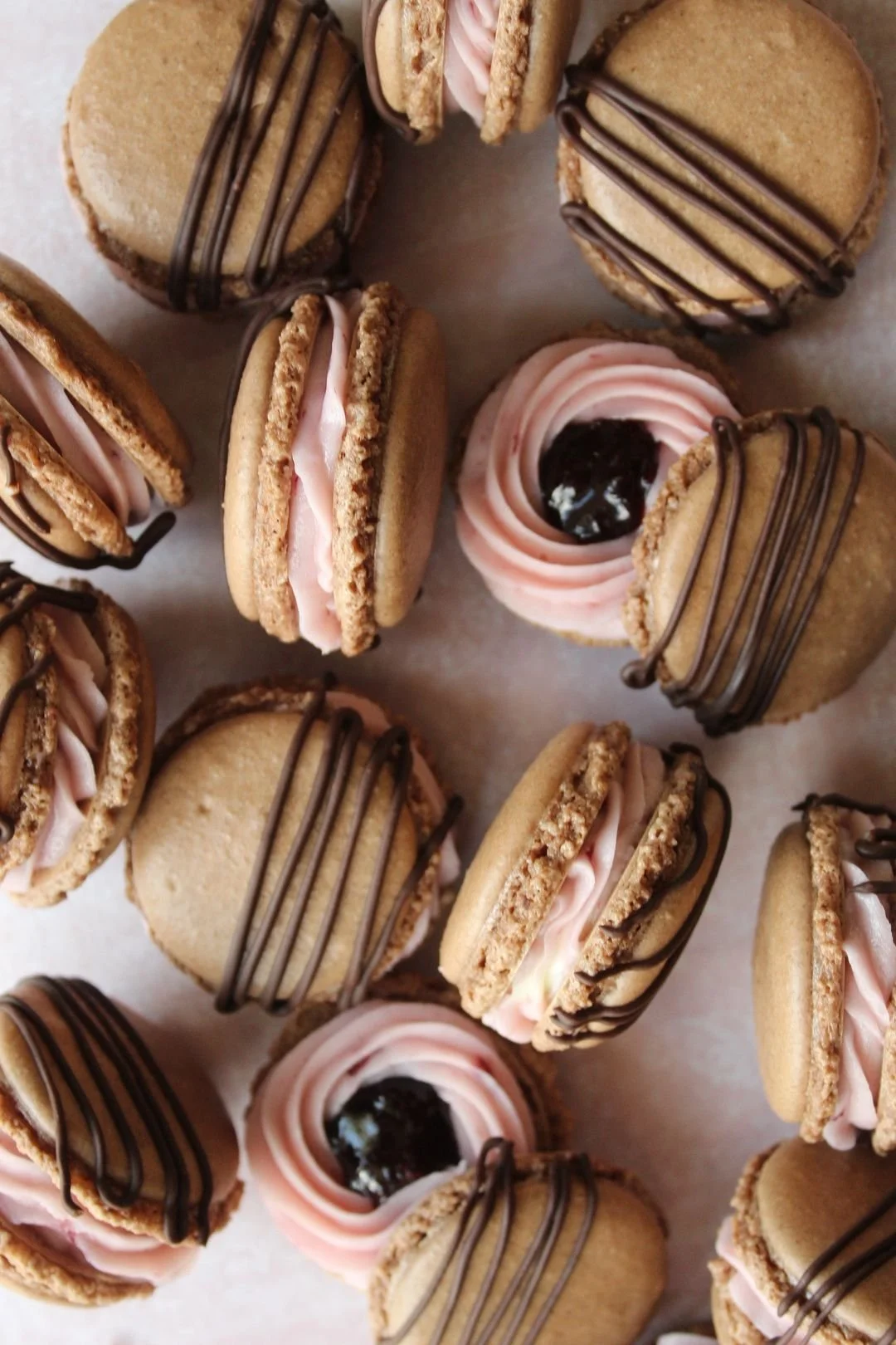 Assorted macarons with pink filling and chocolate drizzle, some topped with cherry jam