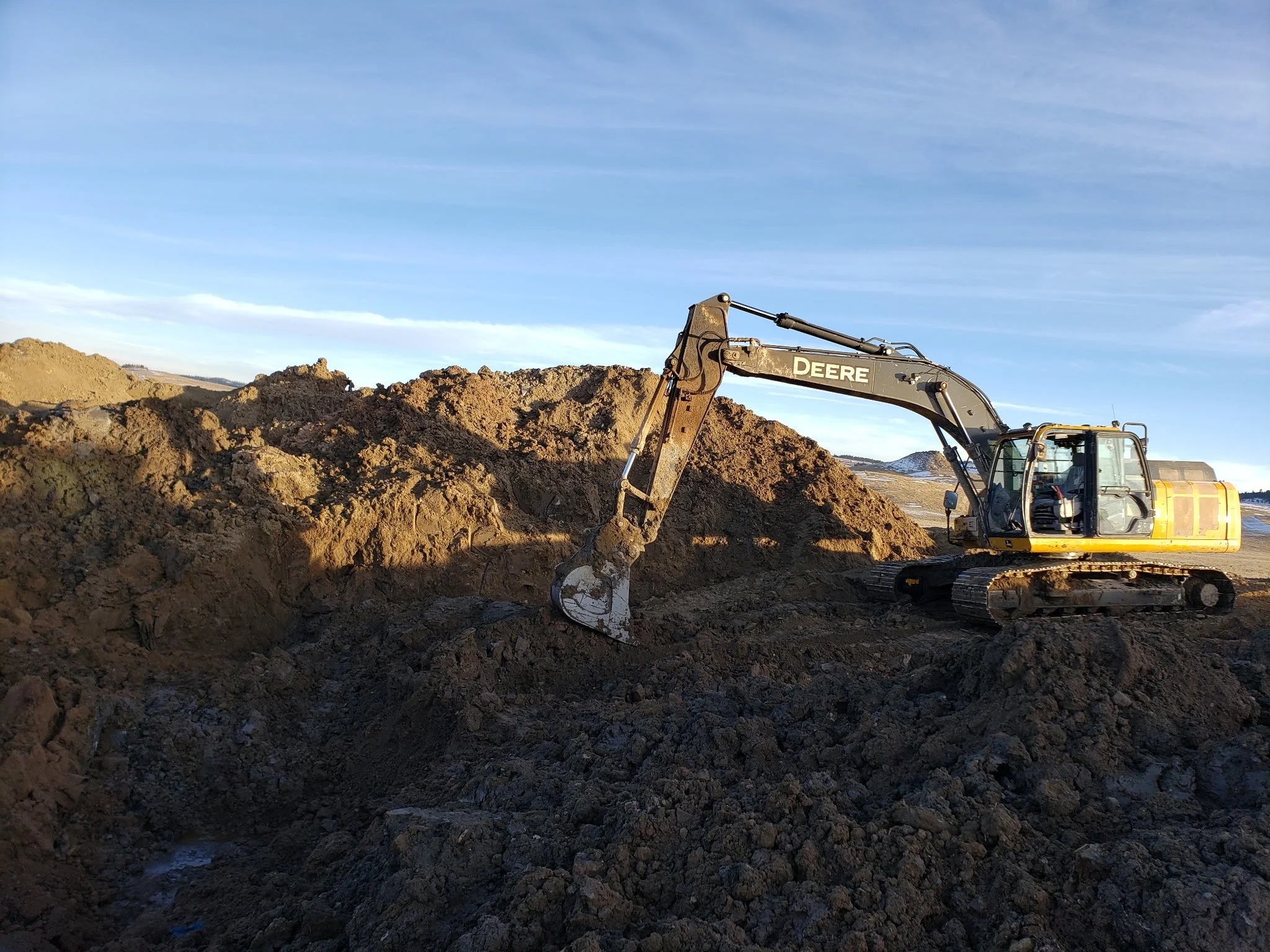 An excavator machine digging and moving dirt in an open construction site with clear blue sky.