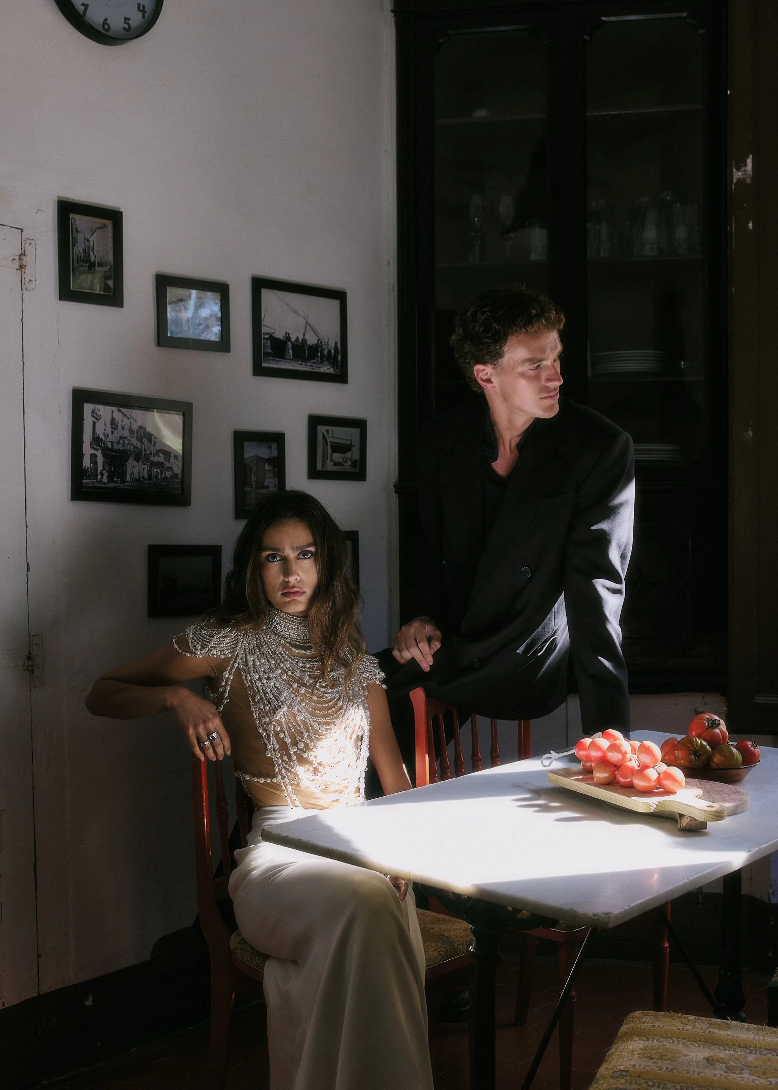 Elena seated at a marble kitchen table with tomatoes as Oscar stands behind her, intimate wedding near Barcelona.