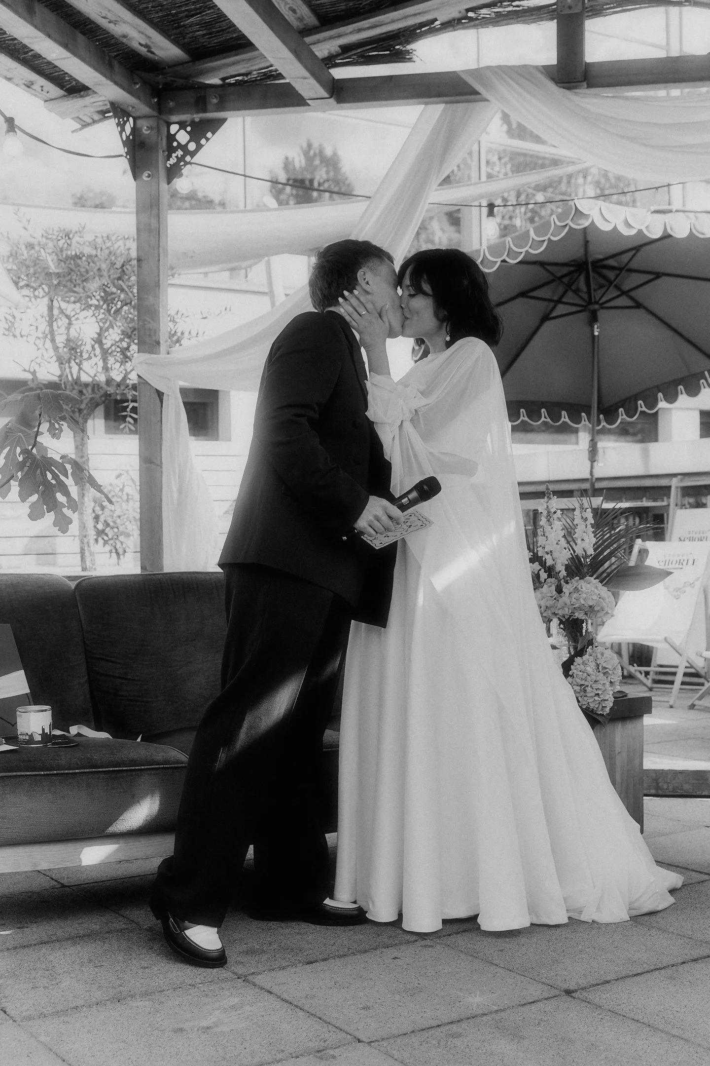Brautpaar küsst sich auf der überdachten Terrasse bei seiner Hochzeit im Hallo Emil Stuttgart, fotografiert in Schwarz-Weiß.