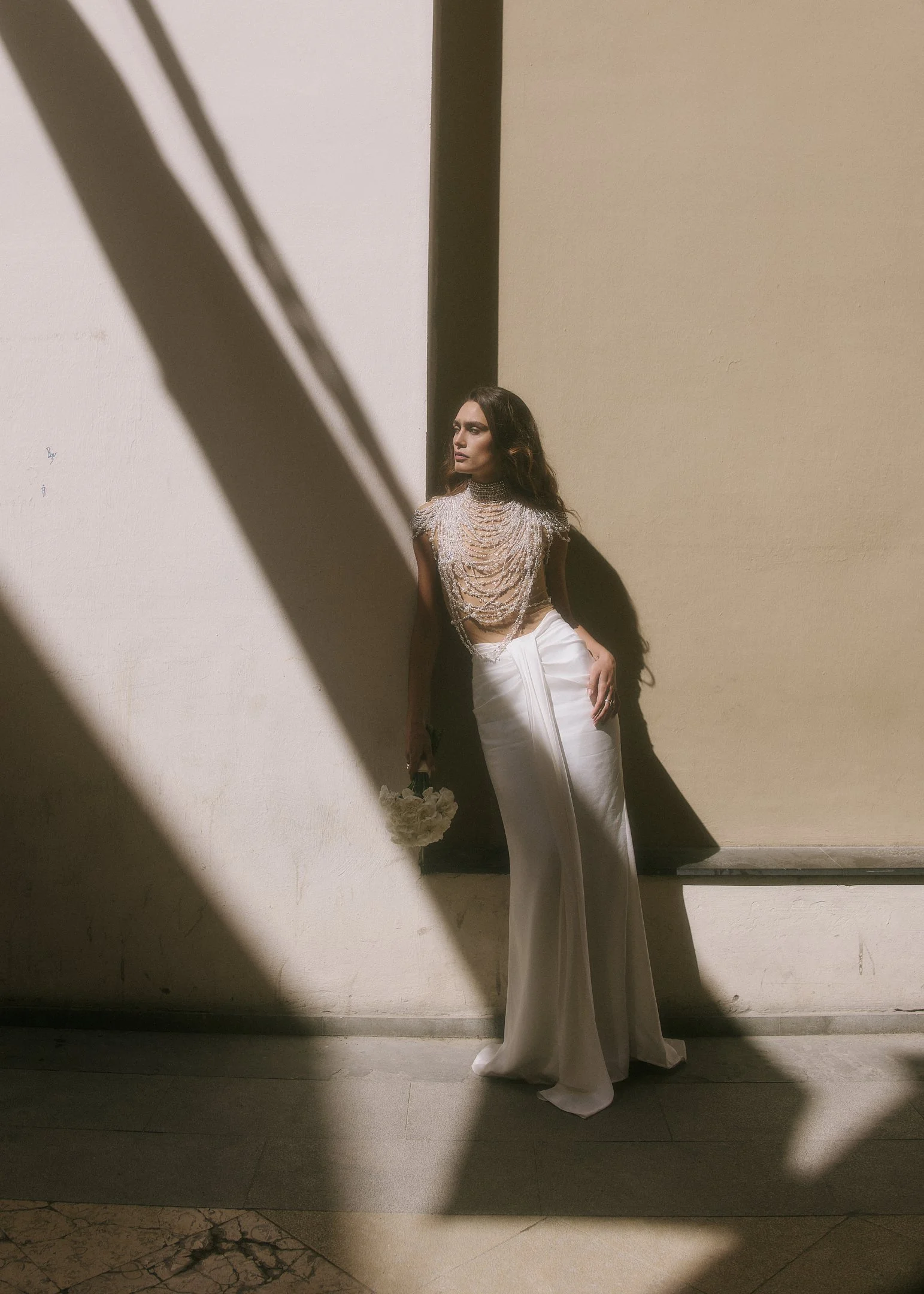 Elena in a white satin skirt against a wall of hard light and shadow, destination wedding photography in Spain.