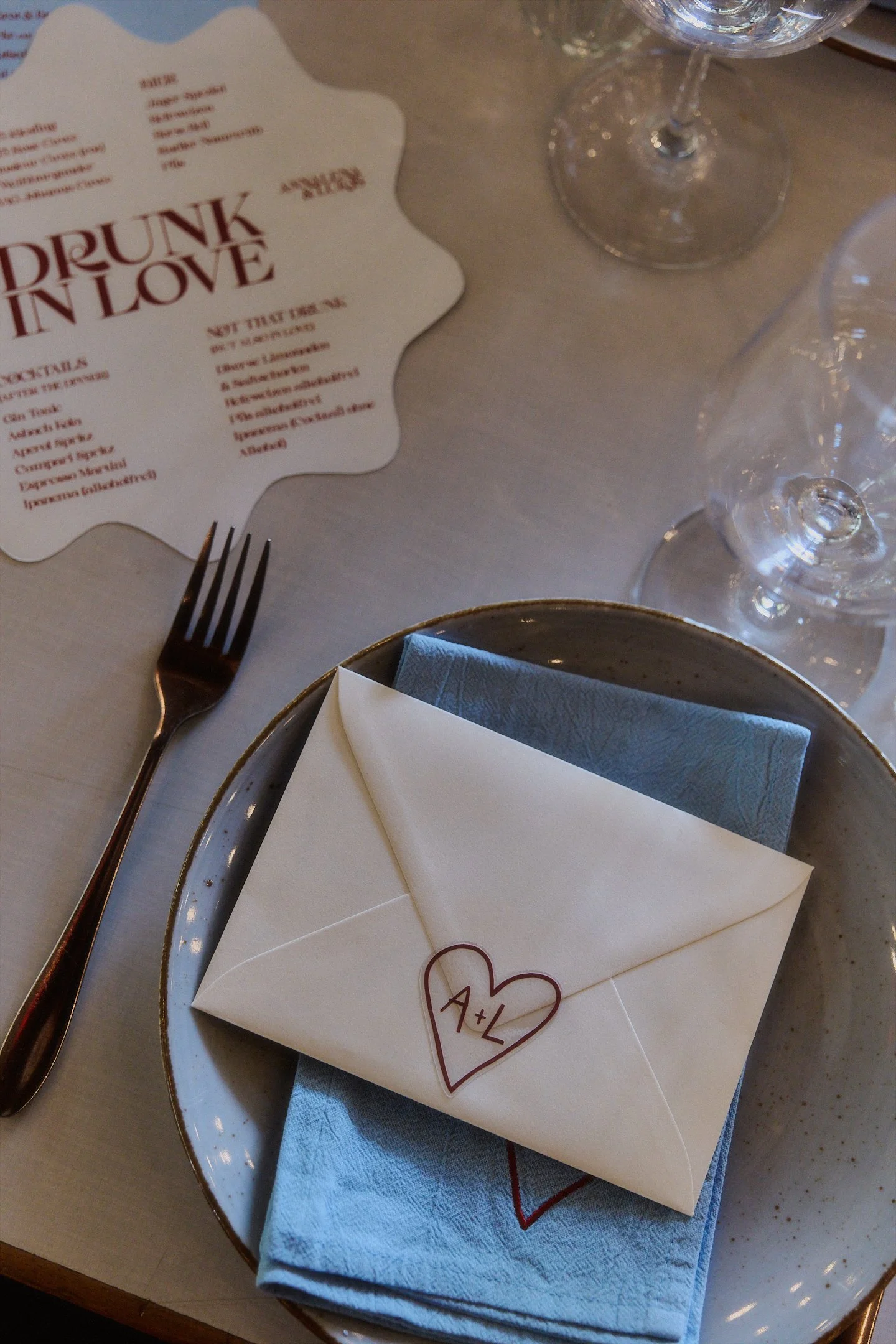 Gedeckter Platz mit blauem Teller, Serviette und einem Umschlag mit Herzzeichnung bei der Hochzeit im Hallo Emil Stuttgart.