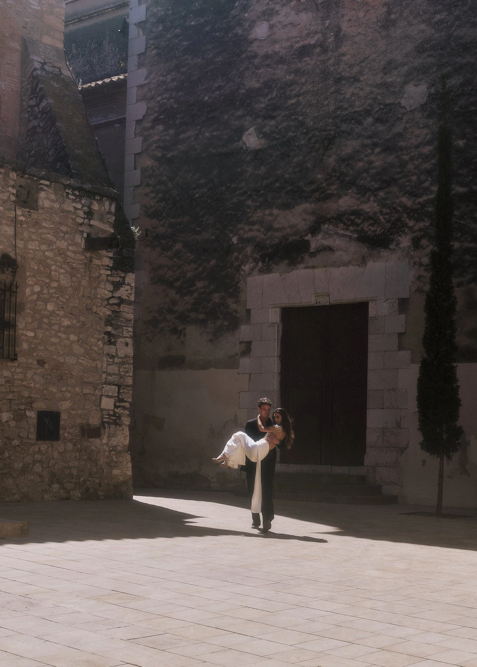 Oscar lifting Elena in a quiet stone square of an old Catalan town near Barcelona.