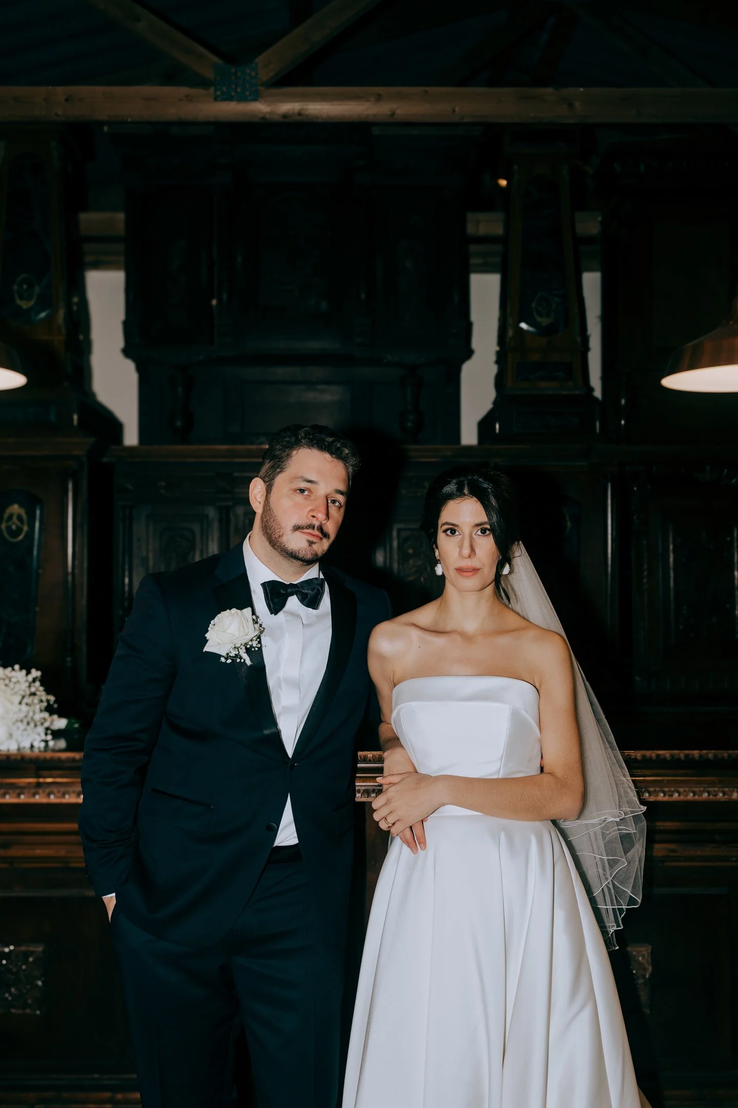 Hochzeitspaar mit Schleier und Fliege vor der dunklen Holzbar im Landgut Steng