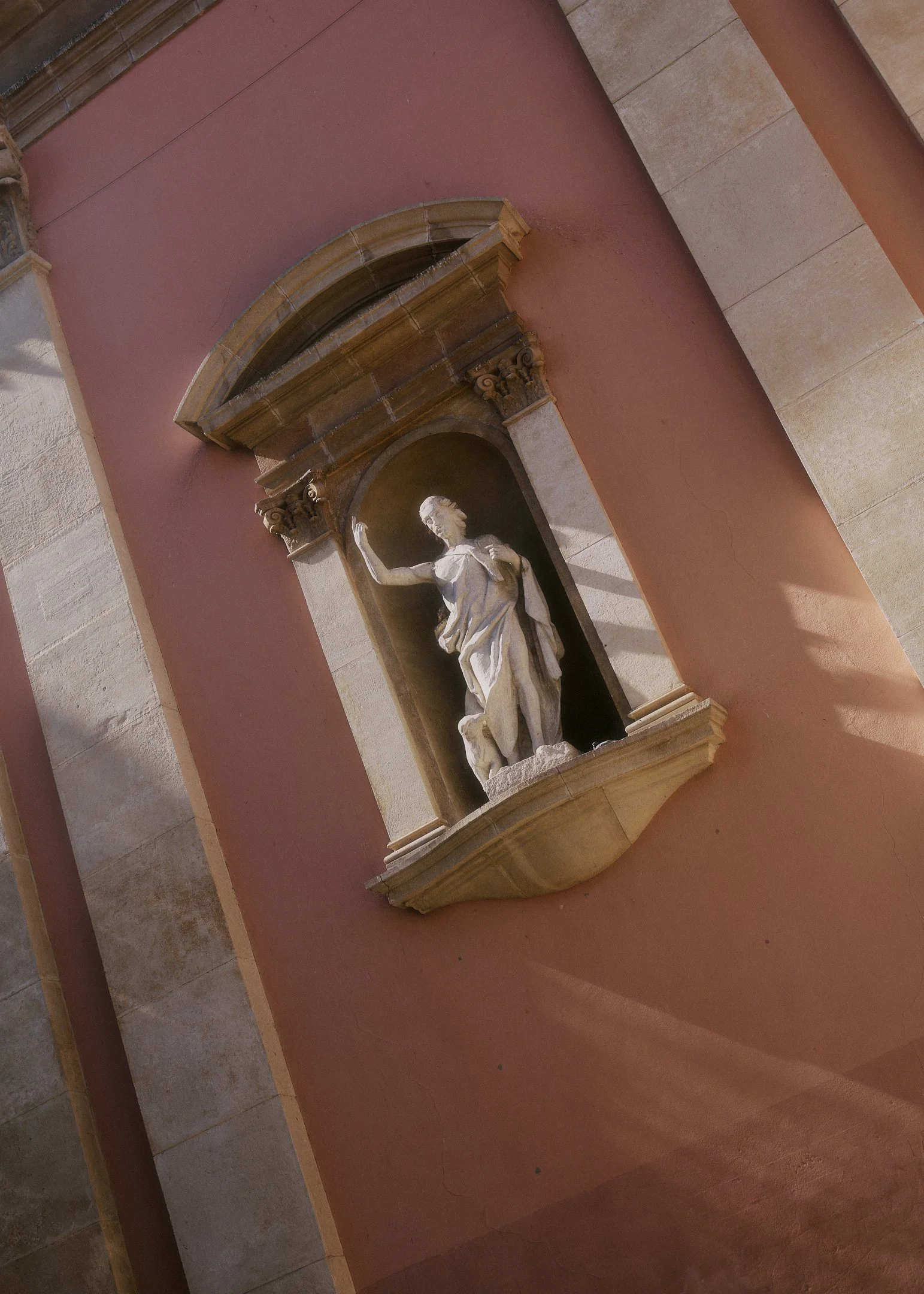 Statue of a saint in a niche on a pink facade in an old town near Barcelona, architectural detail.