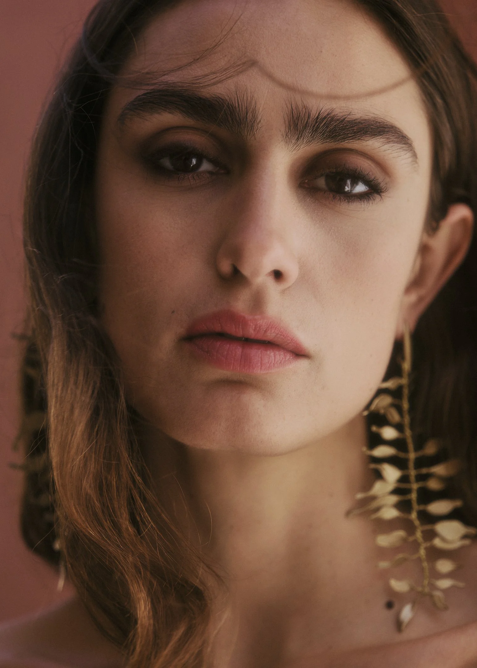 Portrait of Elena wearing a golden leaf headpiece by sach Atelier against a terracotta wall near Barcelona.