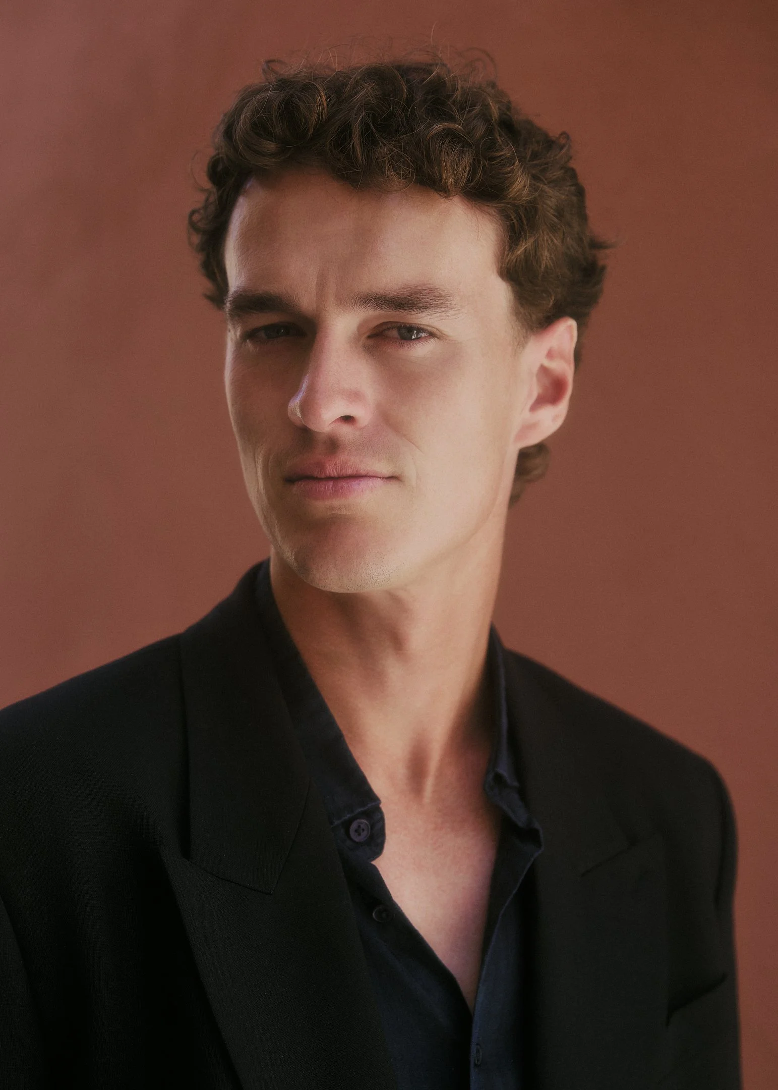 Portrait of Oscar in a black suit against a terracotta wall, groom portrait at a destination wedding in Spain.