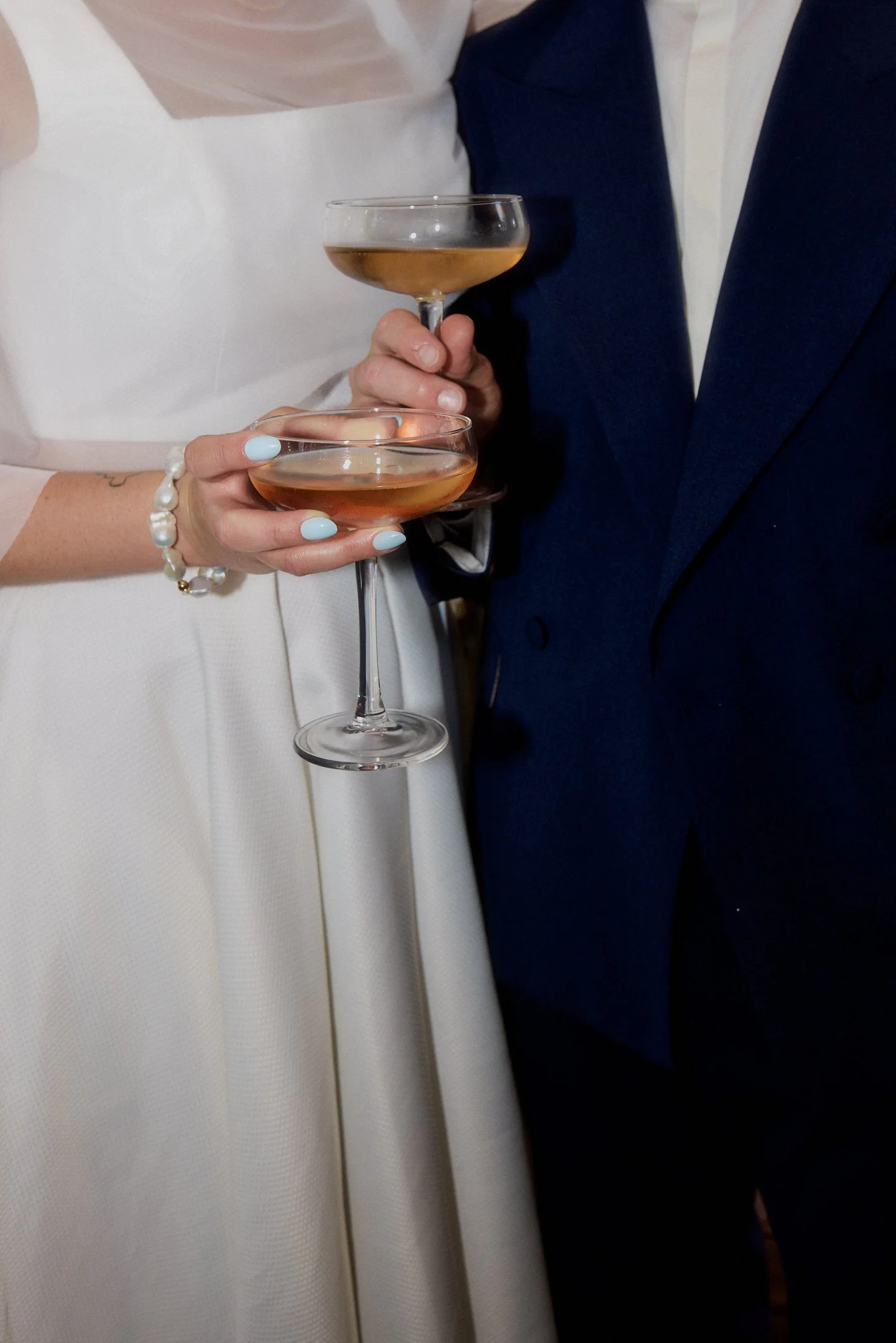 Brautpaar hält zwei Cocktailschalen vor weißem Brautkleid und dunkelblauem Anzug bei seiner Hochzeit im Hallo Emil Stuttgart.