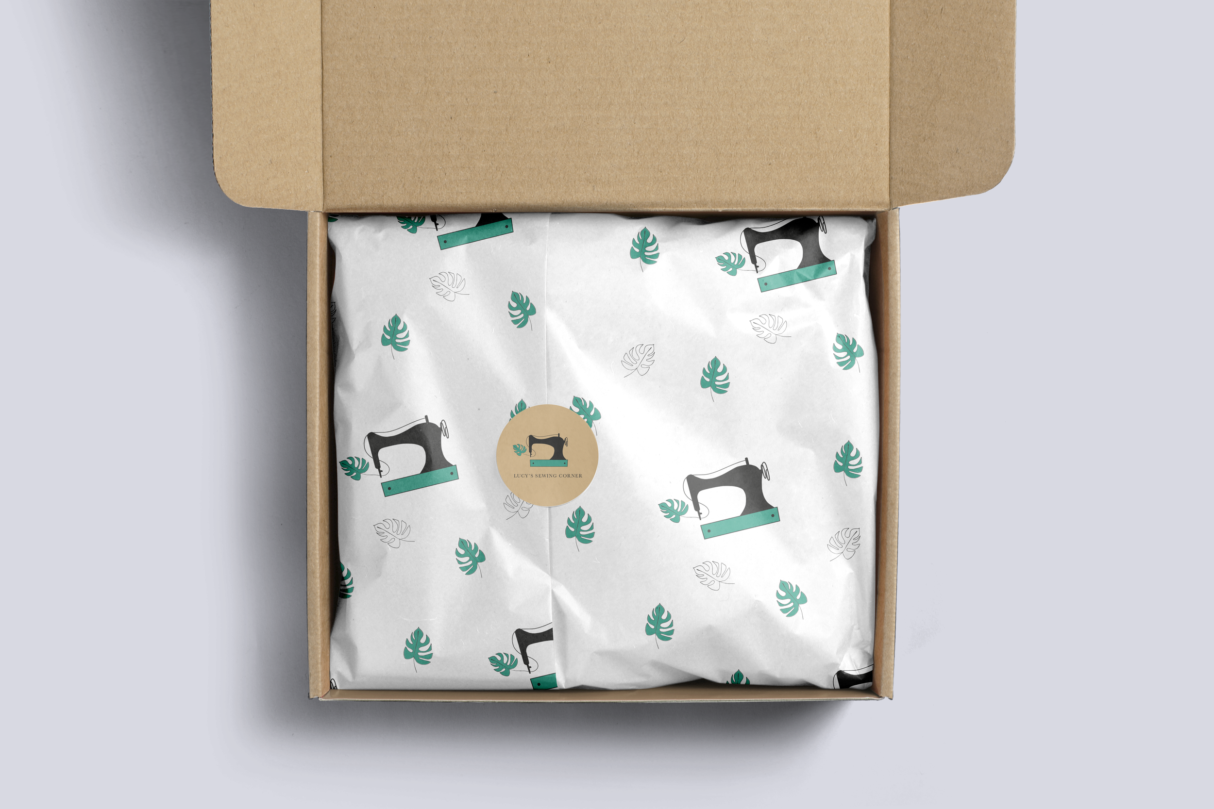 Open cardboard box with patterned wrapping paper featuring black sewing machines, teal leaves, and black and teal rulers.