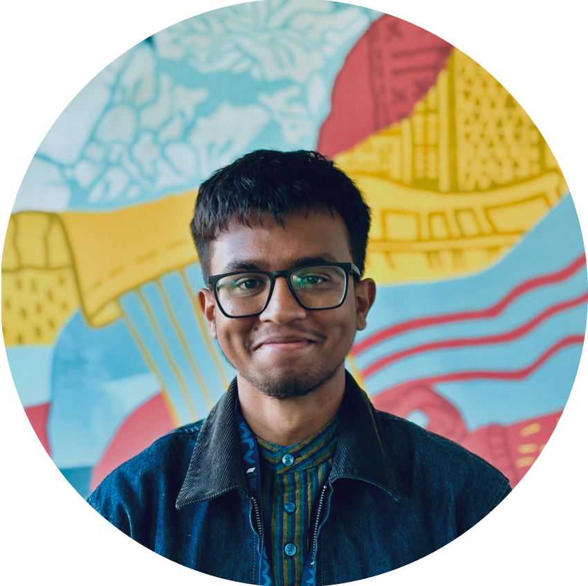 A young man named Arvin, with glasses smiling in front of a colorful mural.