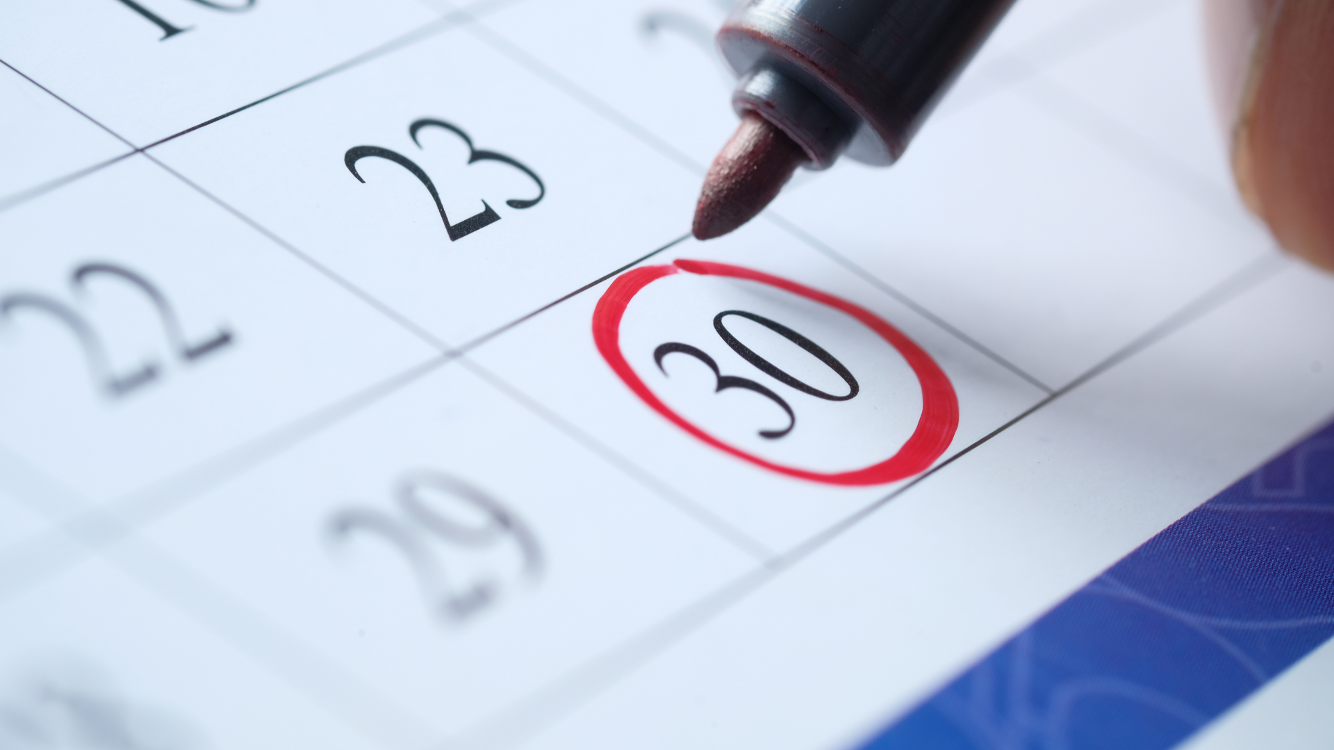 A close-up of a calendar page showing the 23rd, with the date 30 circled in red and being written with a red marker.