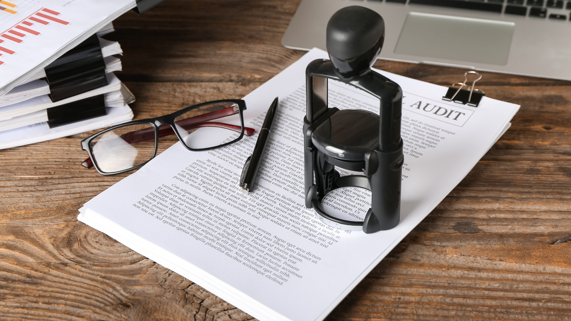 Desk with legal documents, glasses, a pen, a stapler, a binder clip, and a laptop.