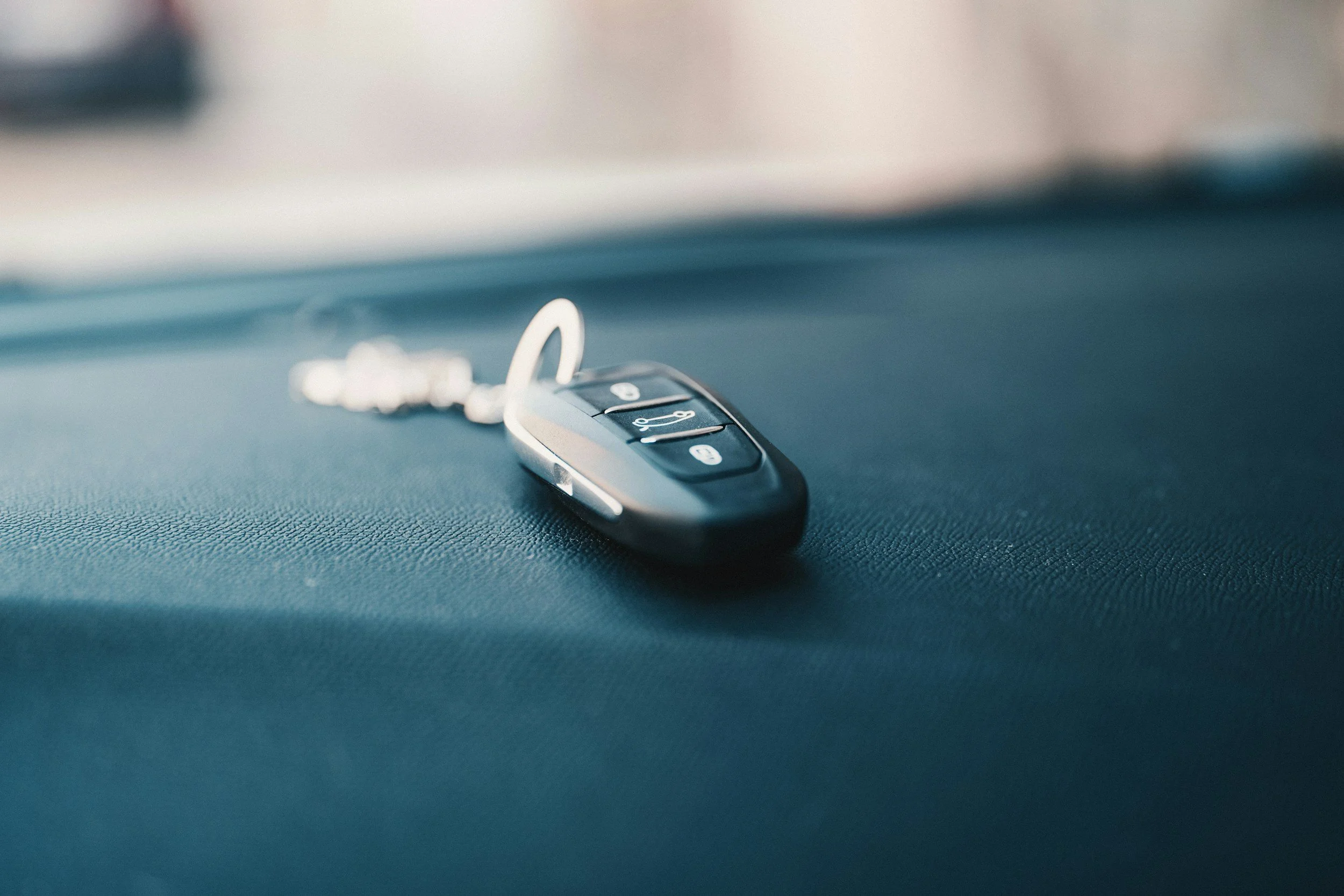 A car key fob with three buttons lying on a textured surface.