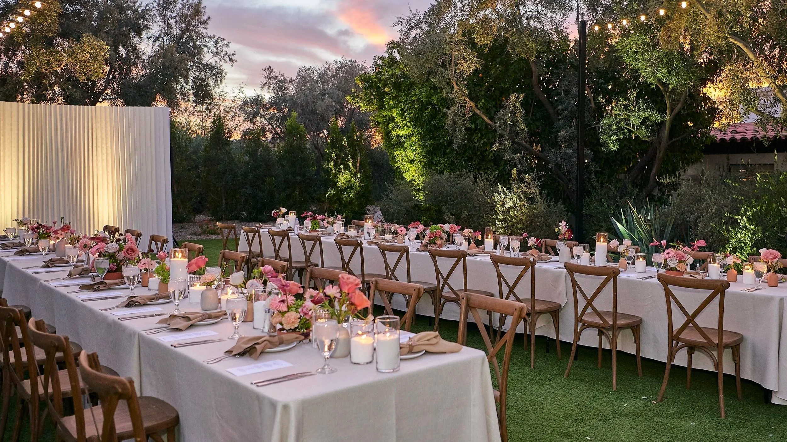 Elegant outdoor dinner with a long candlelit table and pink floral arrangements at sunset